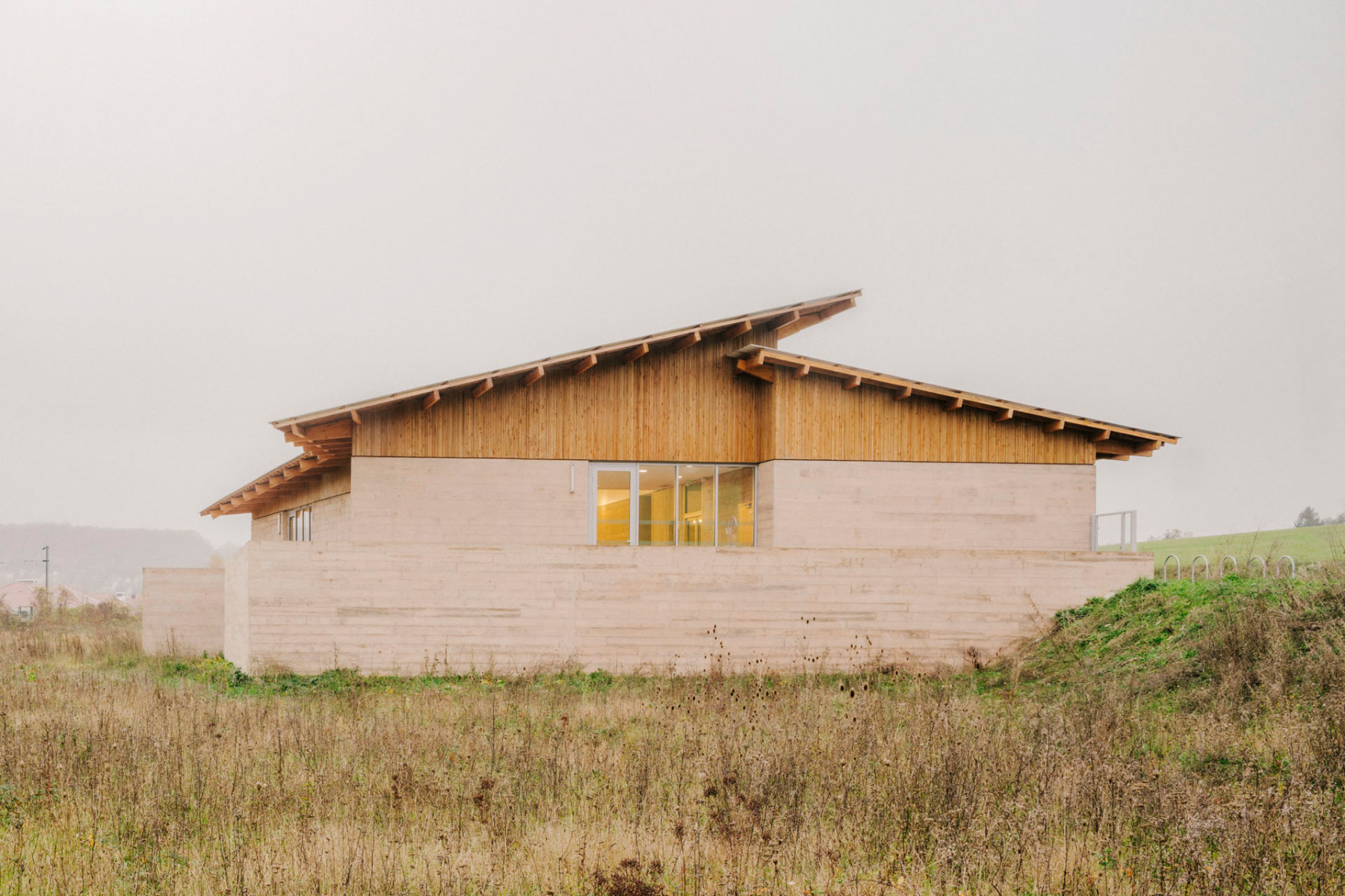 Zwei gegeneinander verschobene Pultdachflächen überspannen den Neubau, der zwischen den Ortsteilen auf dem freien Feld liegt. © Maxime Verret