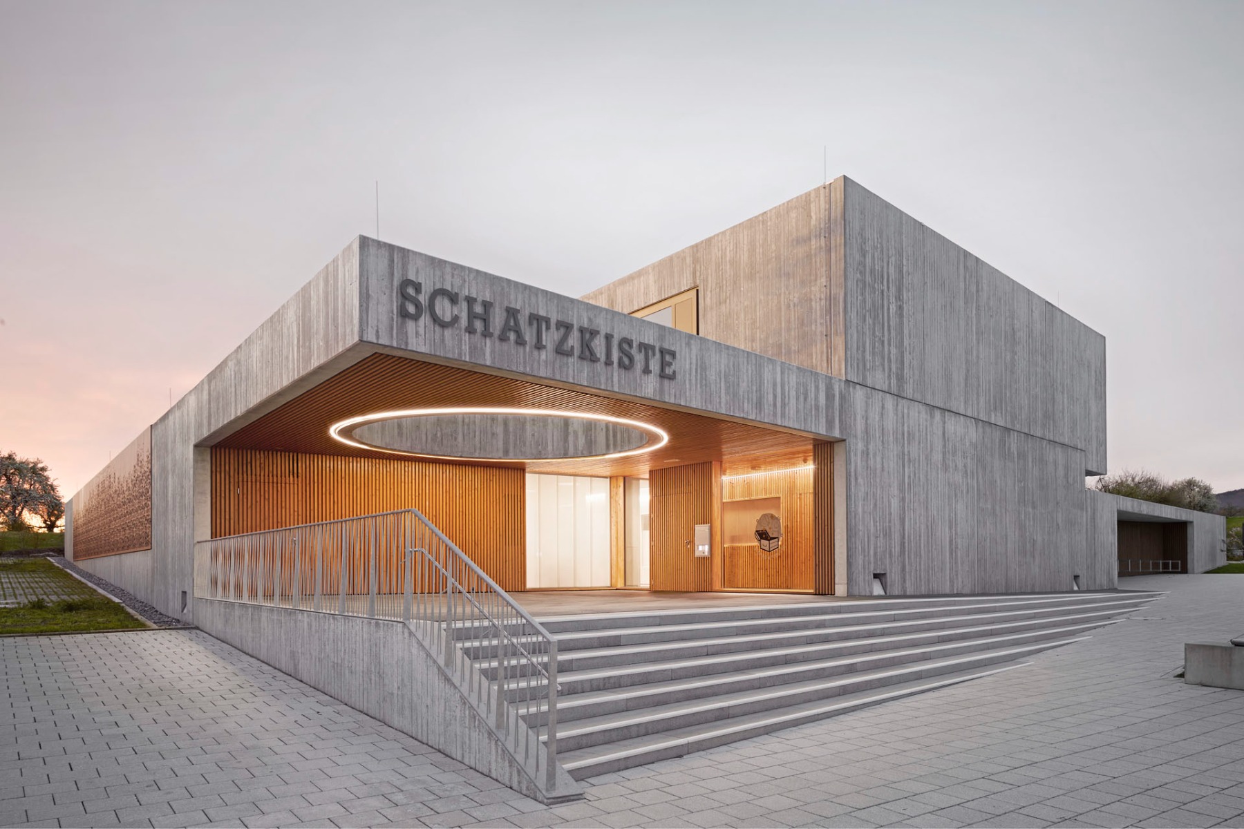 Von Sichtbeton gerahmt: Der in einem Rücksprung platzierte Eingangsbereich der Kita empfängt die Kinder mit viel Holz und einem kreisrunden Himmelsausschnitt. © Julian Bauer