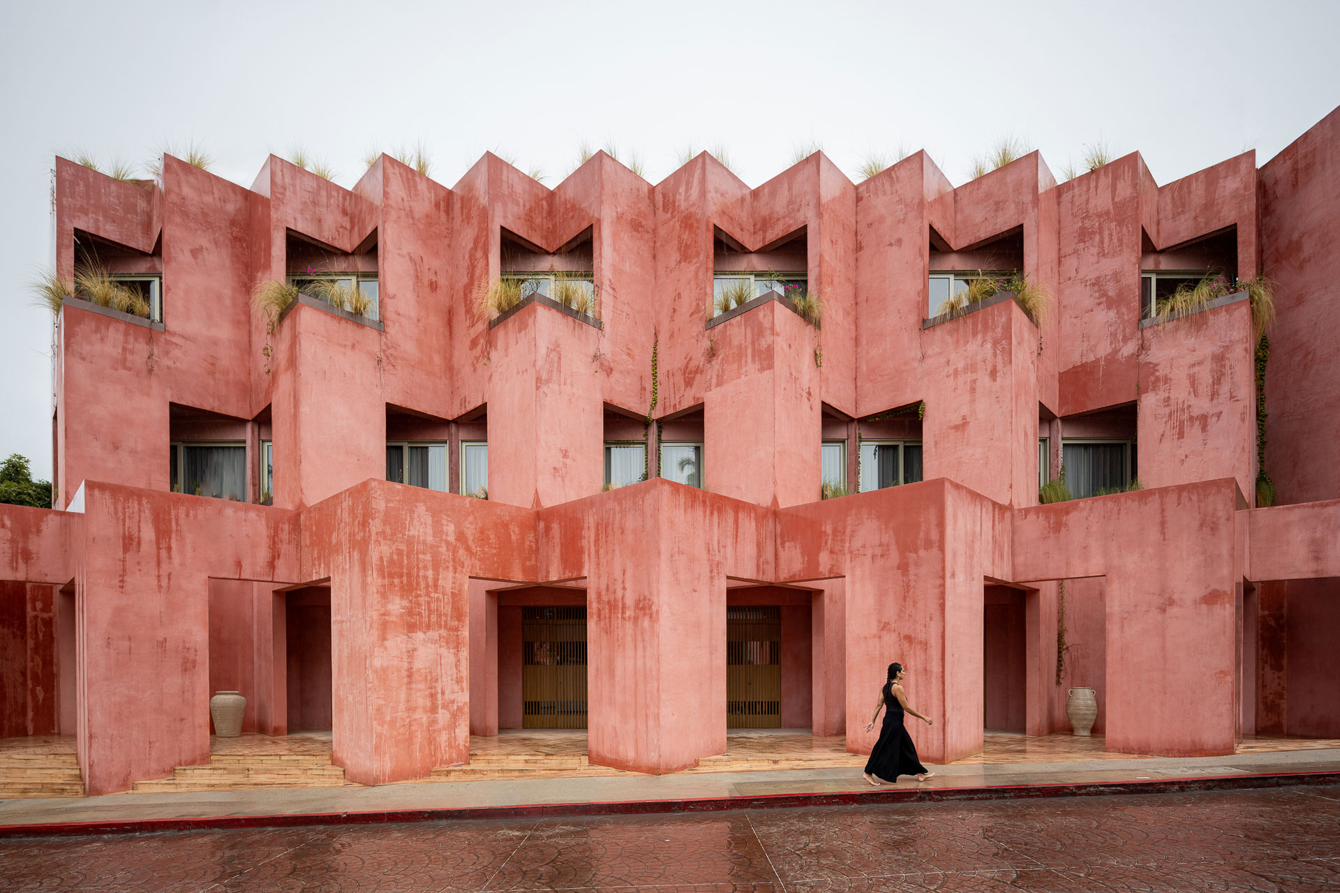 Die gefaltete Betonfassade leuchtet in kr&auml;ftigem Rot. Das Bauwerk schmiegt sich an die leichte Steigung der Stra&szlig;e. &copy; Oscar Hern&aacute;ndez