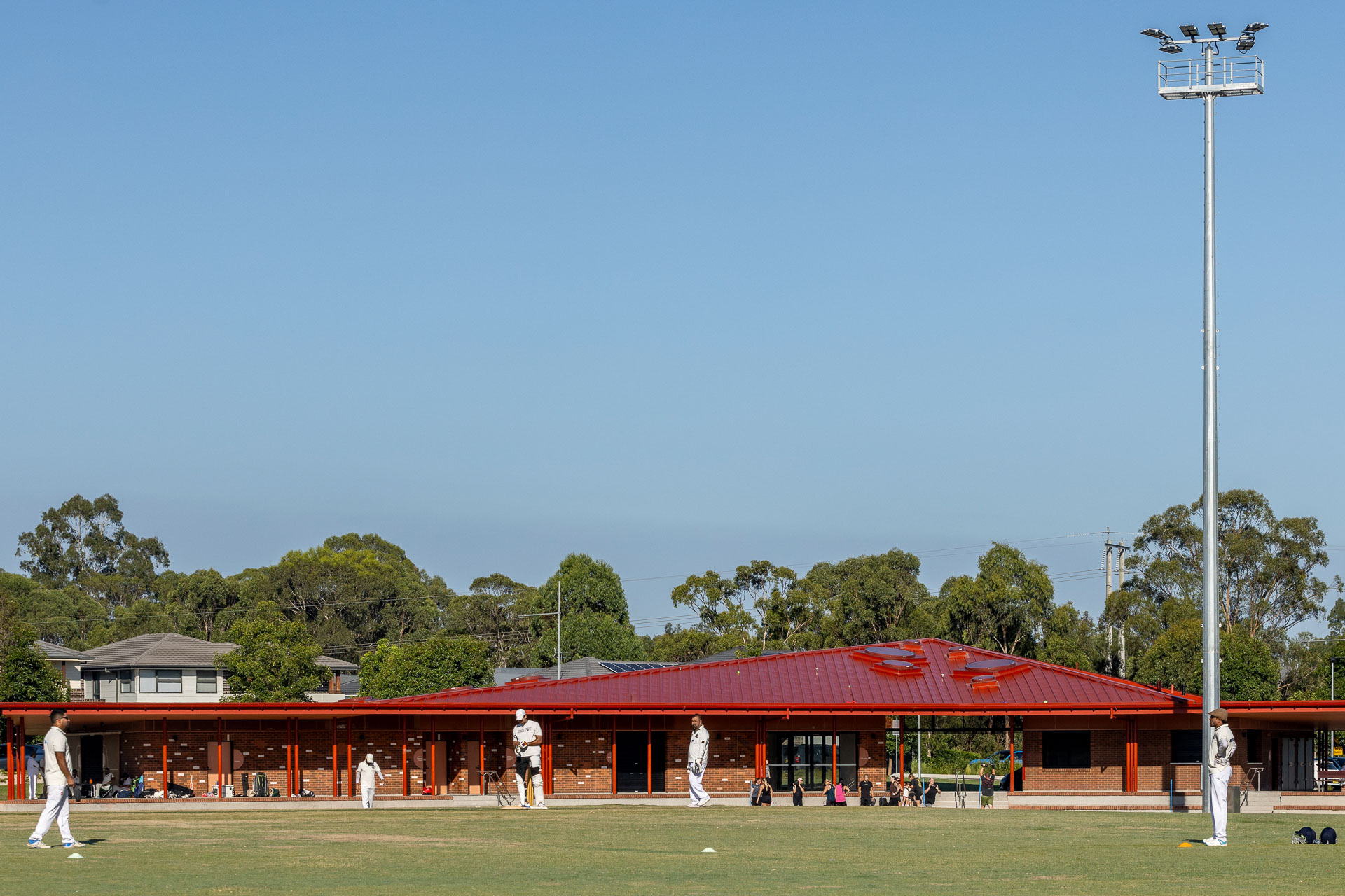 Mit leuchtend rotem Dach empf&auml;ngt der eingeschossige Pavillon seine Besucher inmitten der gr&uuml;nen Sportfl&auml;che. &copy; Brett Boardman 