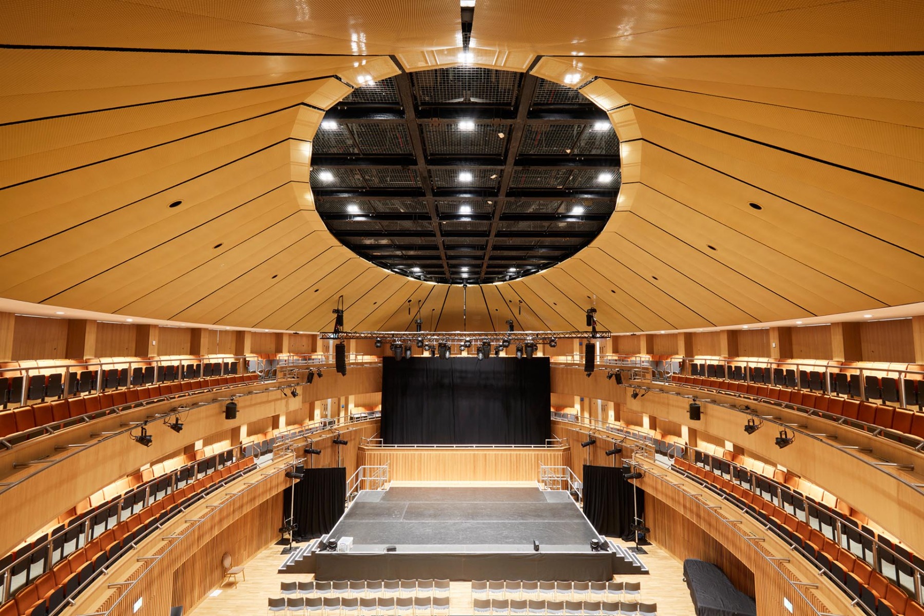 Das Architekturgewebe PC-Alu 6020 optimiert in der St. Edwards School in Oxford die Akustik. Das goldbronzefarbene Finish setzt die Farbgestaltung des Saals an der Decke fort. © GKD Group