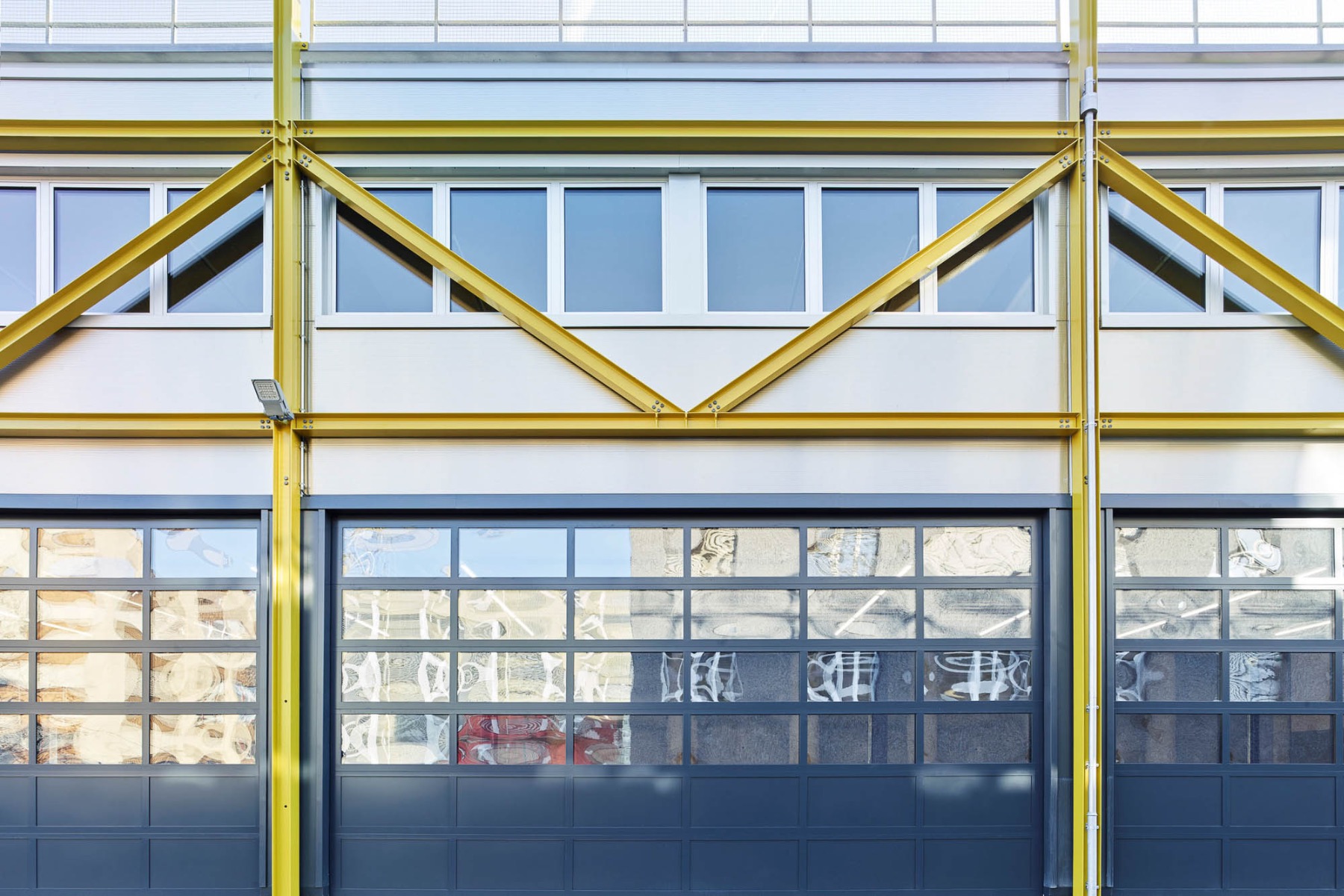 Die Fassade des neuen Werkhofs für das Unternehmen Energie Opfikon in Zürich zeichnet sich durch dunkle Garagentore, silberne Fassadenelemente und gelbe Windverbände aus. © Markus Bertschi Fotografie, Zürich