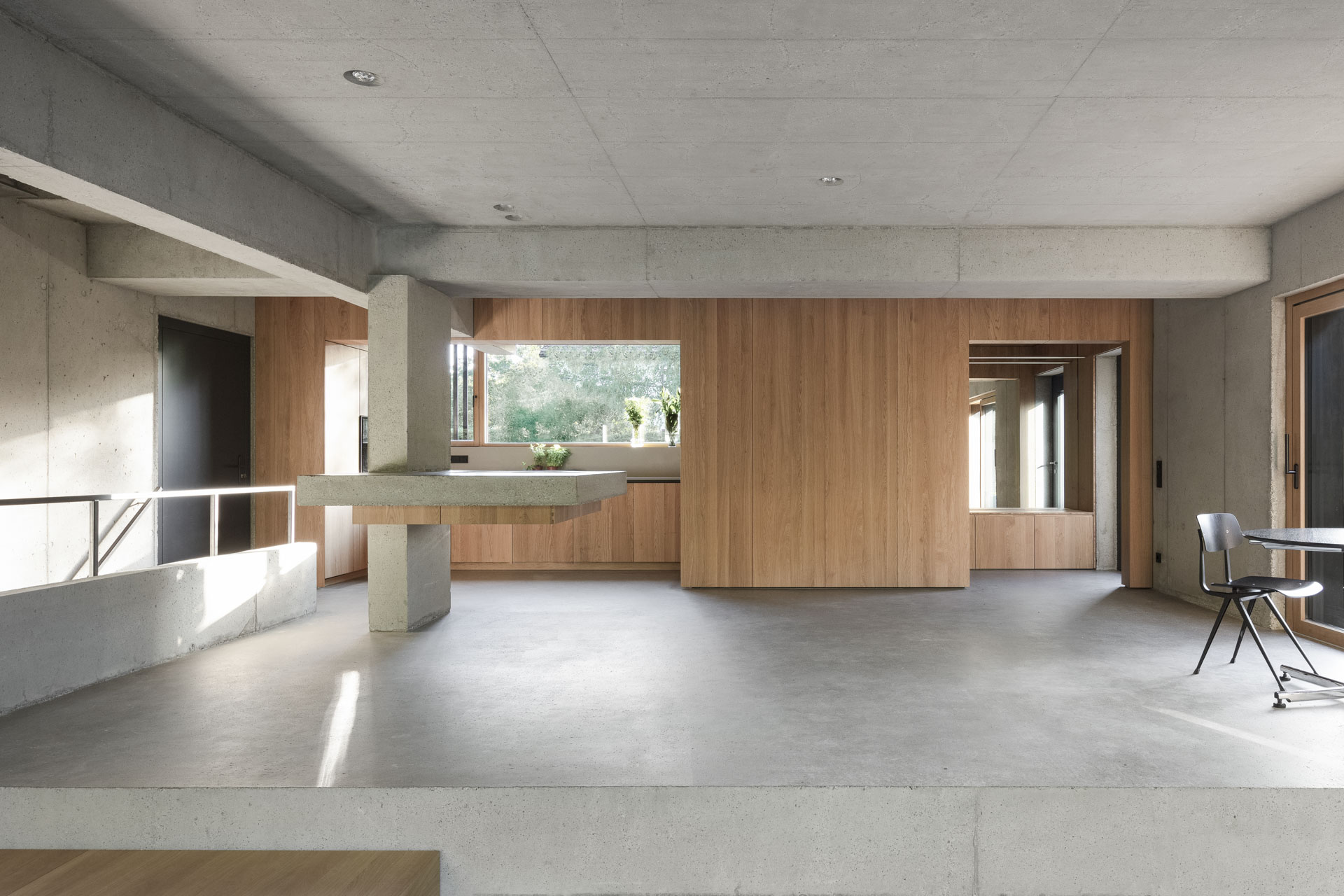 Großzügiger Wohnraum mit Sichtbeton und Holzverkleidung. Integrierte Küche in offenem Grundriss.