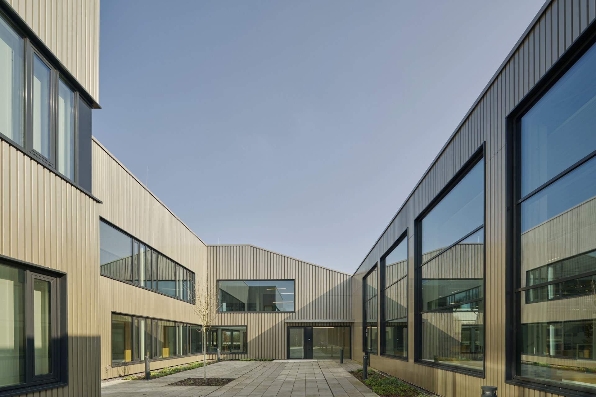 Innenhof eines modernen Bürogebäudes mit metallverkleideter Fassade, großen Fensterflächen und klarer geometrischer Formensprache.