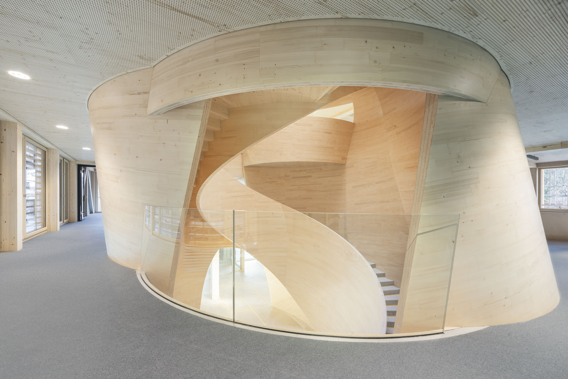 Eine geschwungene Holztreppe als skulpturales Element im Gebäudeinneren.