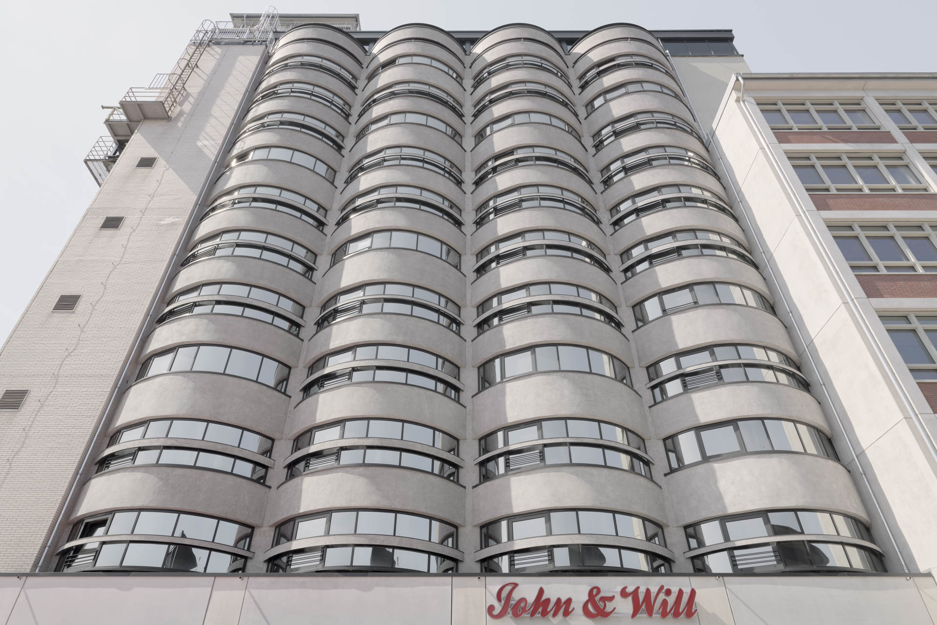 Fassade von unten, vertikal strukturierte Betonfront mit vier halbrunden Tonnen, horizontale Fensterschlitze, brutalistischer Industriecharakter.