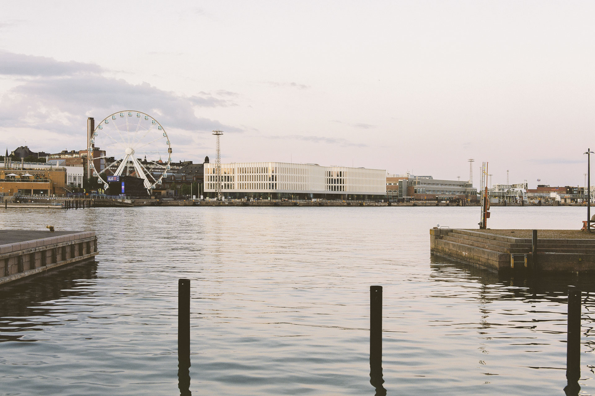 Blick über das Wasser auf Uferbebauung mit Riesenrad und modernem weißen Gebäude mit großflächigen Verglasungen.