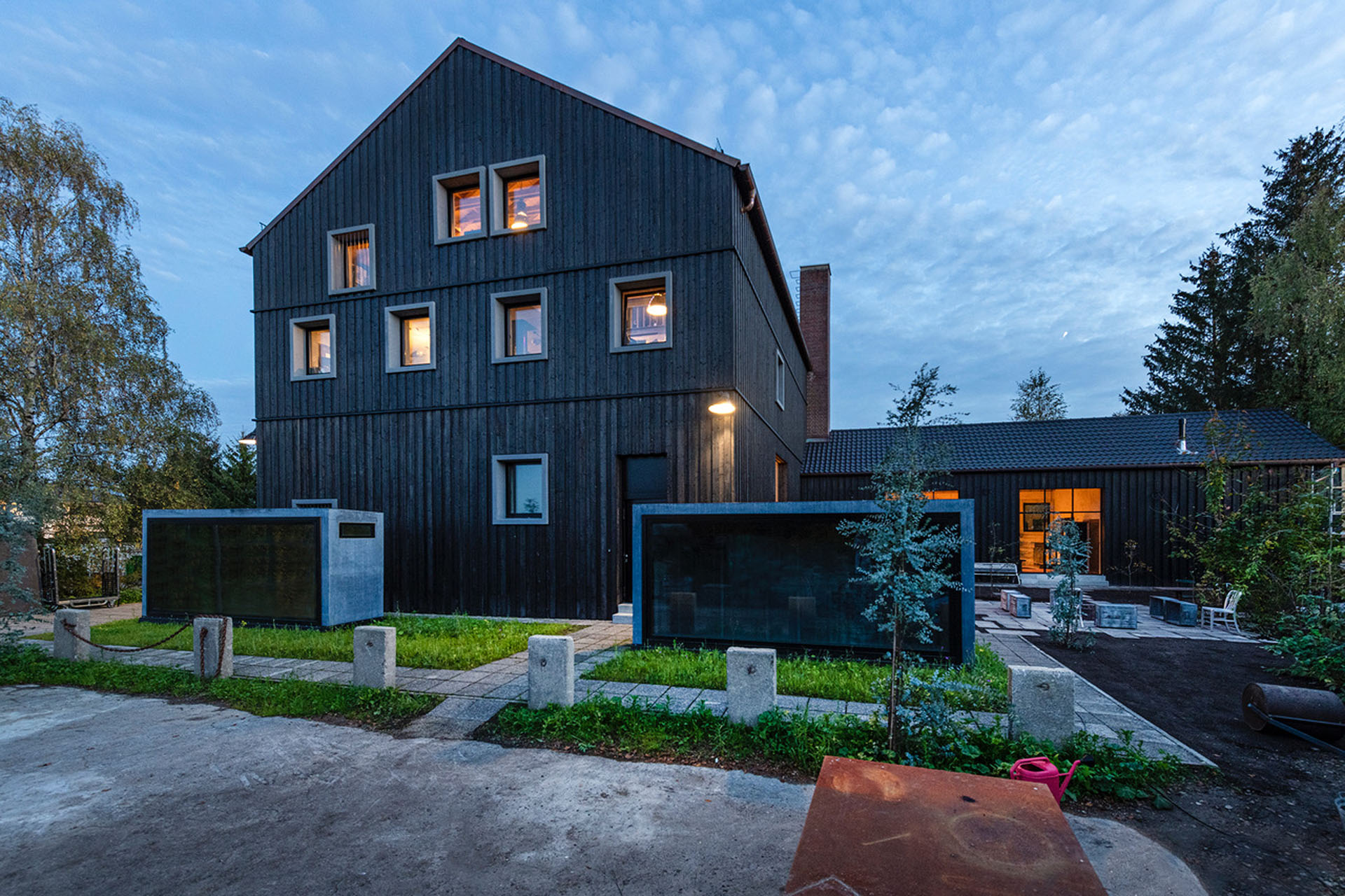 Außengelände einer ehemaligen Schnapsbrennerei mit holzverkleidetem Haus und Anbau in der Abenddämmerung.