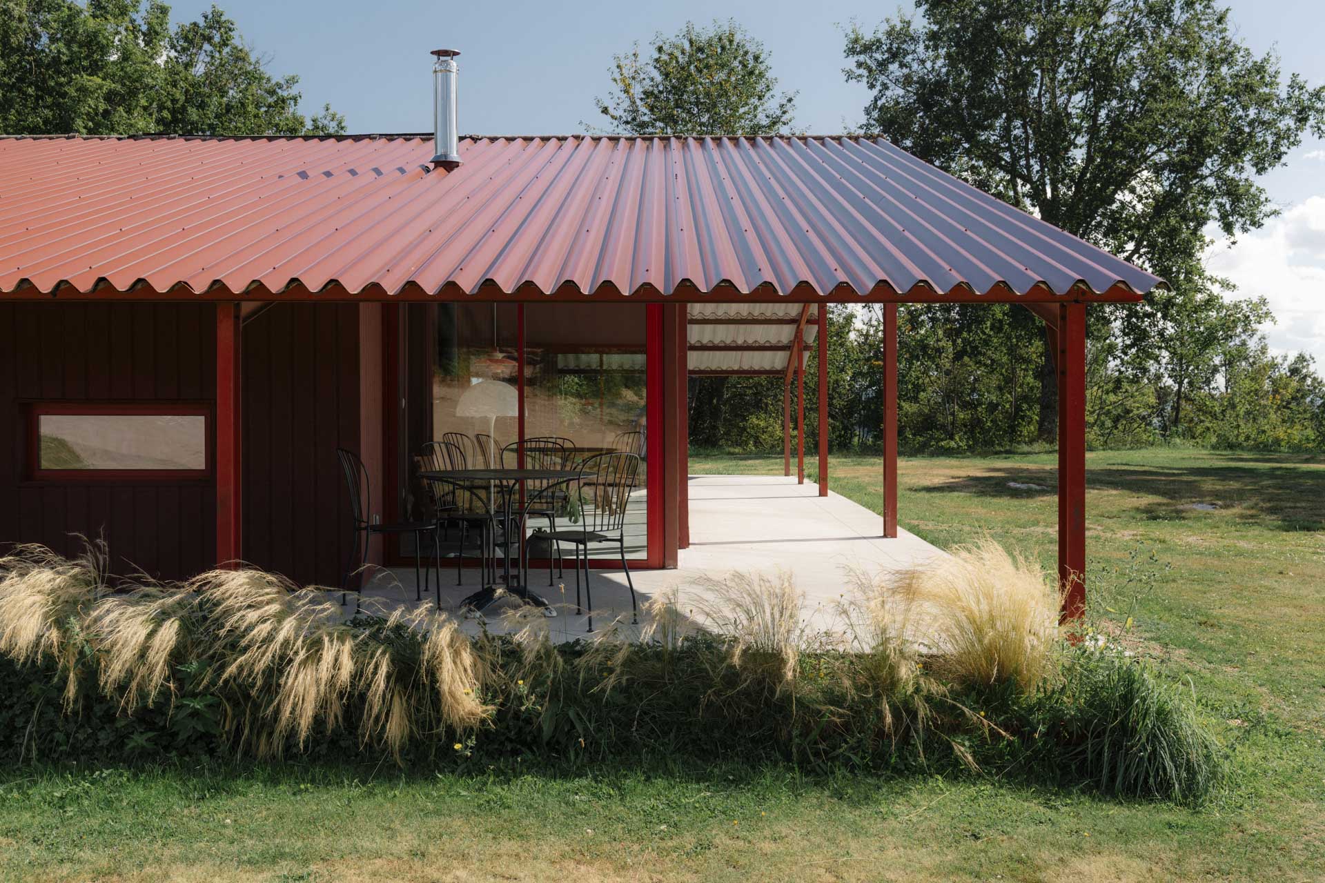 Roter Bungalow mit Metall- und Holzfassade auf großzügigem Rasengrund, Terrasse öffnet sich zum Garten.