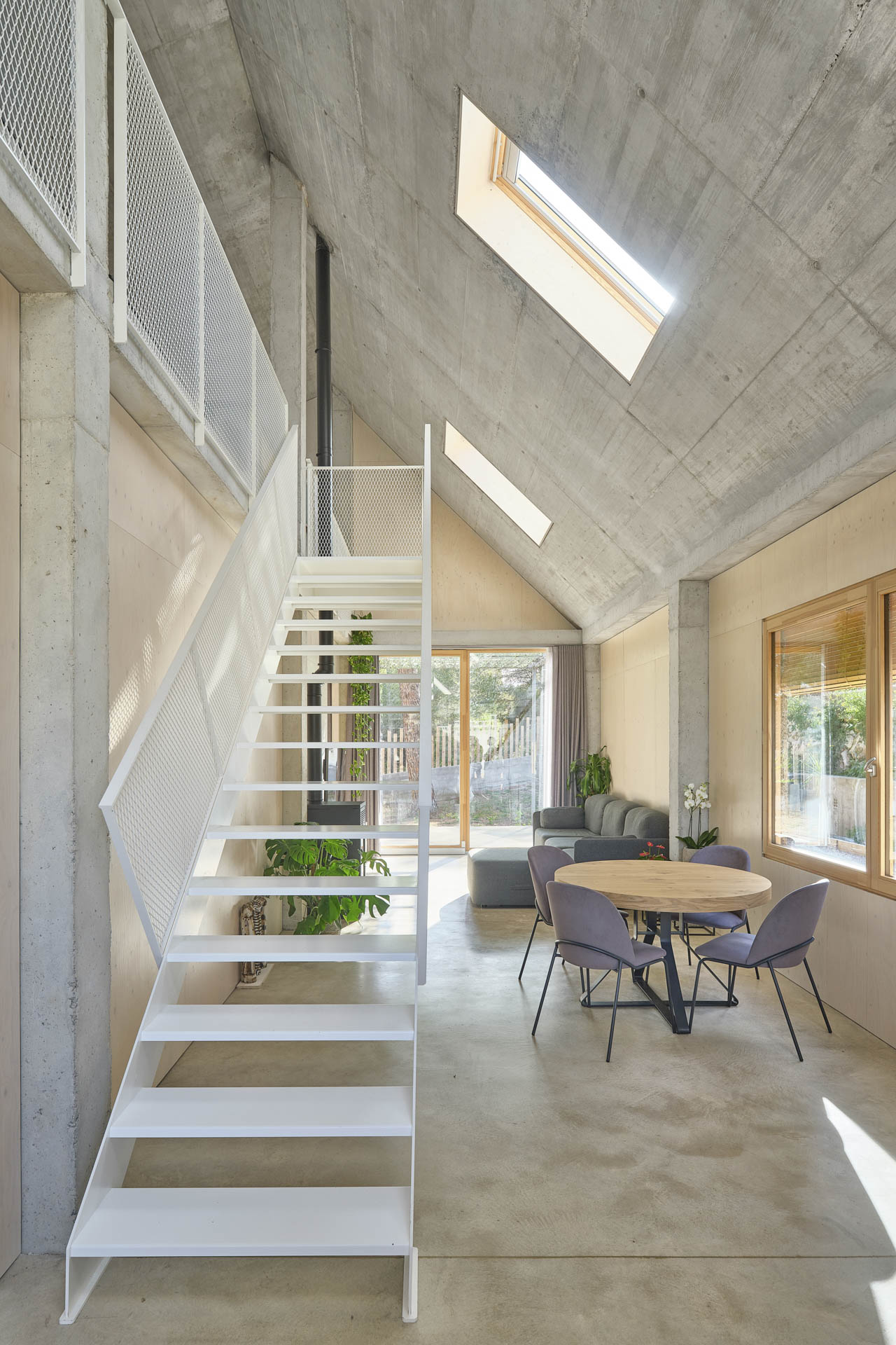 Doppelgeschossiger Innenraum mit Wohnlandschaft und weißer Metalltreppe zum Obergeschoss.