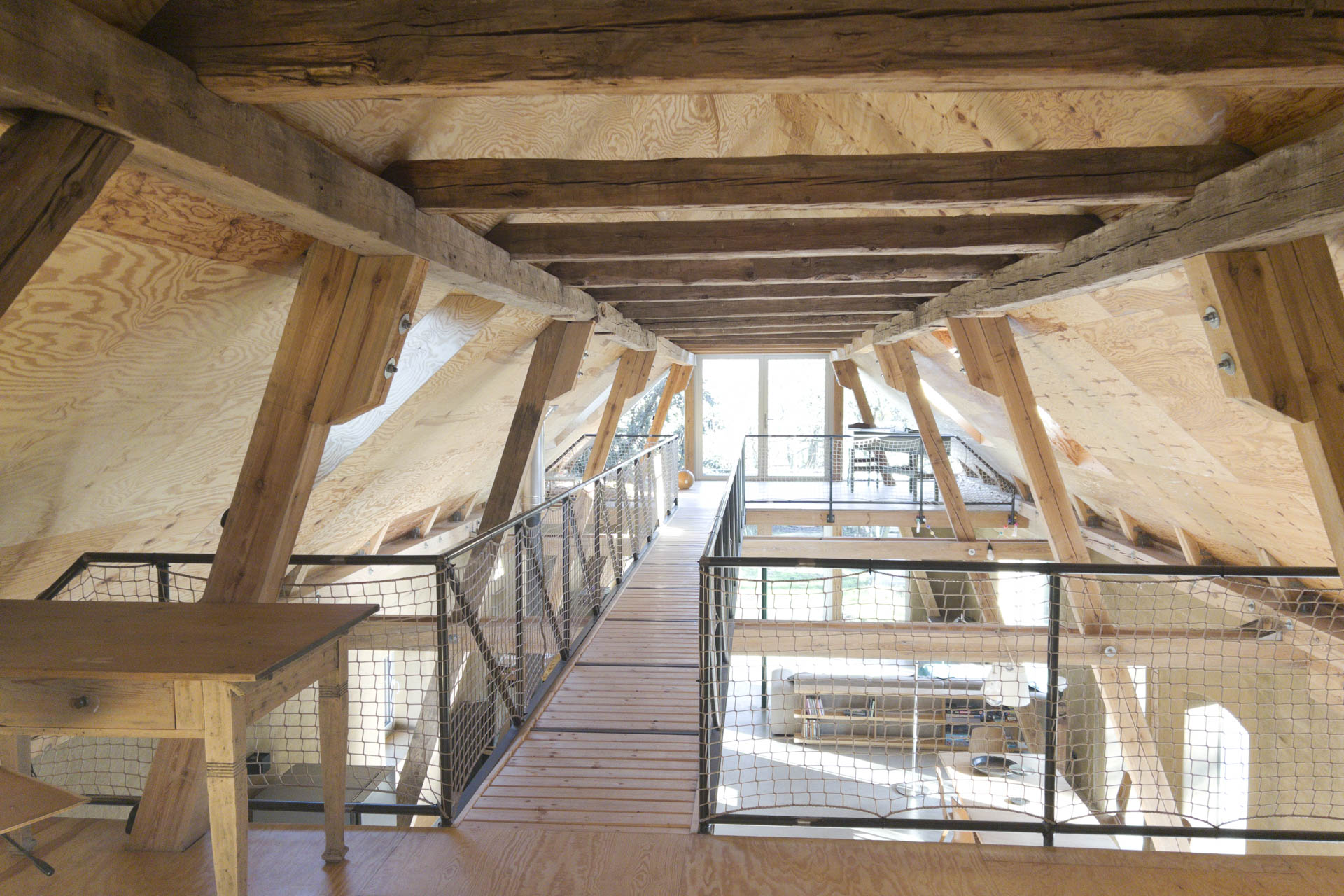 Holzdachstuhl mit teilweiser Zwischendecke und Steg, verglaste Giebelfront, darunter offener Wohnraum im Untergeschoss.