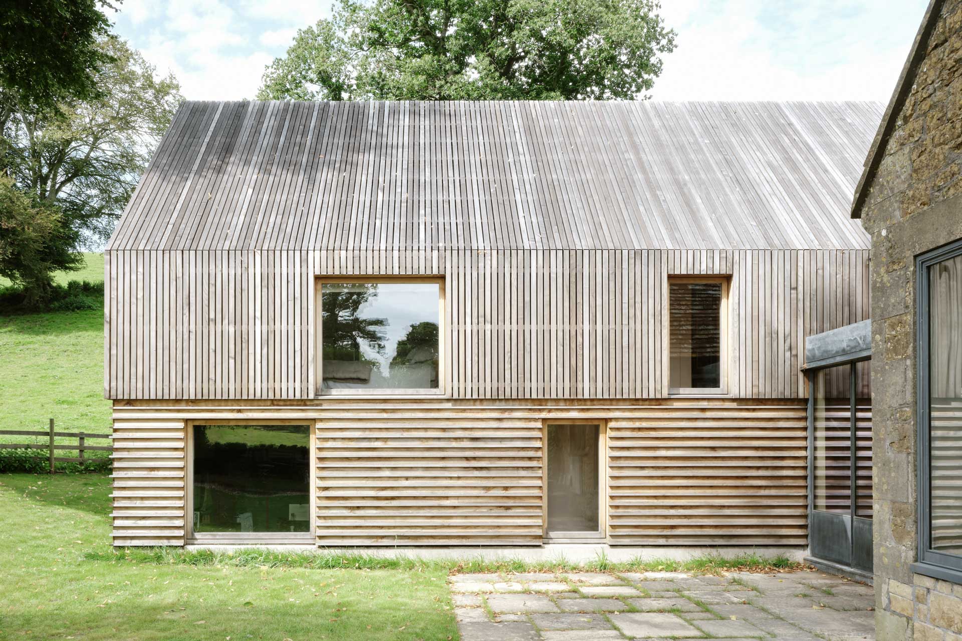 Anbau mit durchgehender vertikaler Holzverschalung an Fassade und Dach. Große Fensteröffnungen, untere Zone mit horizontaler Lattung.
