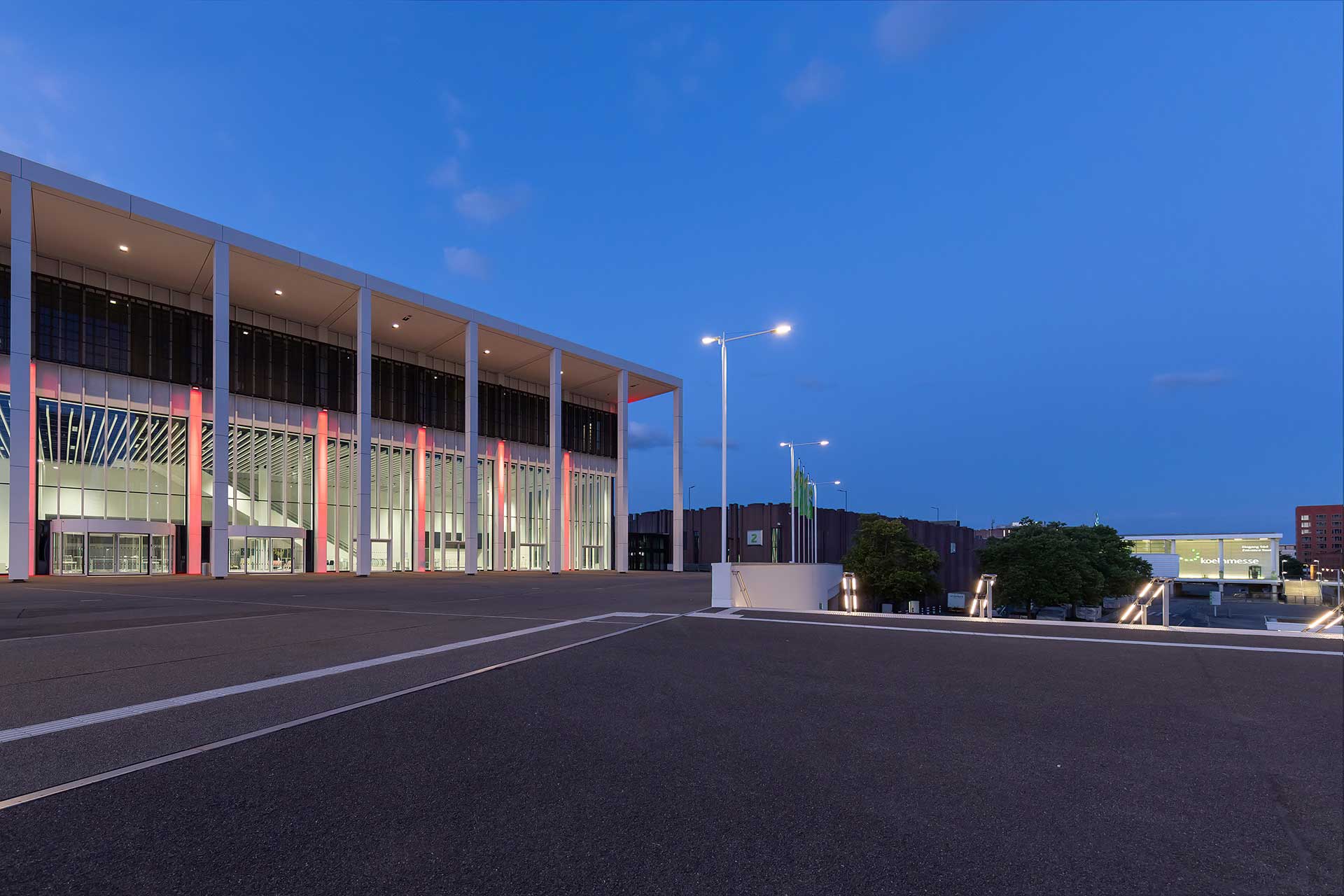 Beleuchtete Messehalle bei Nacht vor einem leeren Platz.