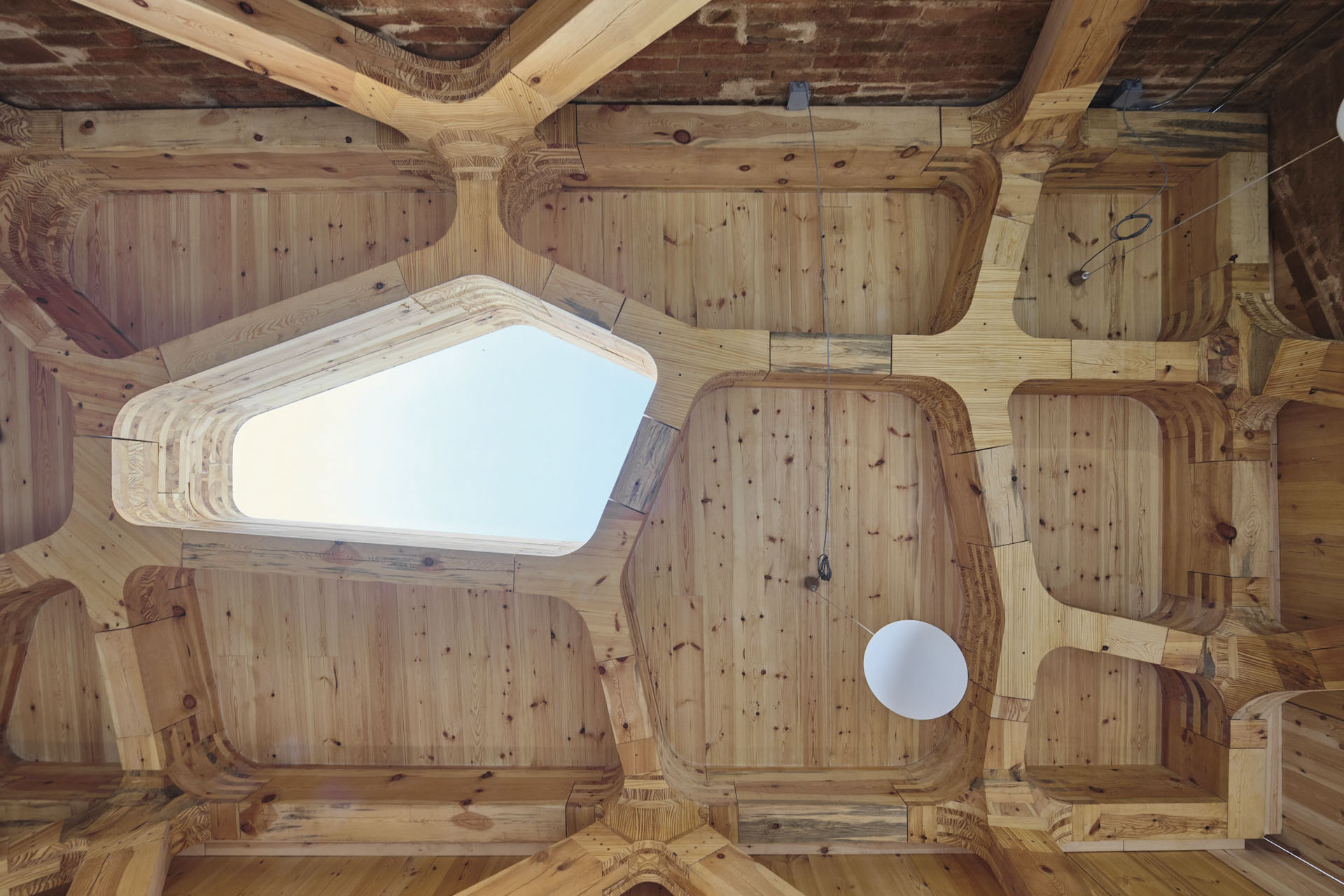 Holzdecke mit komplexer, gefräster Tragwerksstruktur und Oberlicht.