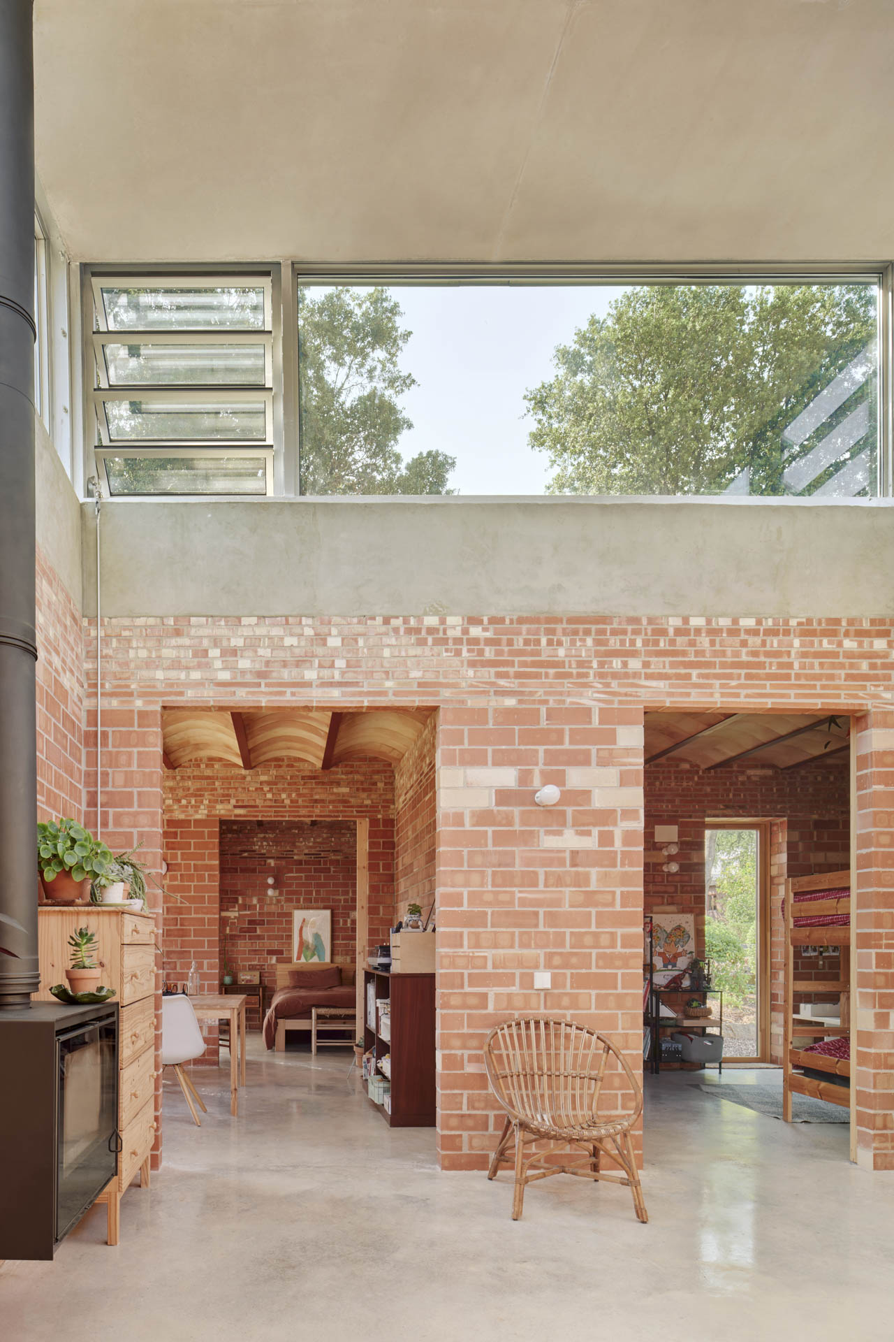 Raum mit Sichtziegelwänden, gewölbter Ziegeldecke und großem Oberlichtband; glatter Betonboden, Stahlrohrkamin und sichtbare Raumdurchgänge.