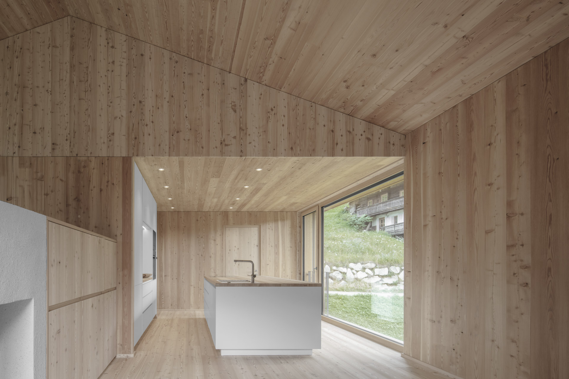 House with light wood facade on concrete base in green hillside location.