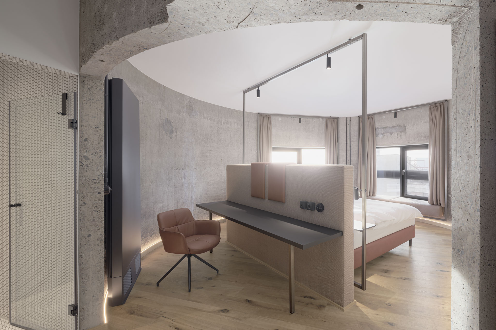 Hotelzimmer mit runder Betonwand, Einschnitt und horizontalen Fensterschlitzen.
