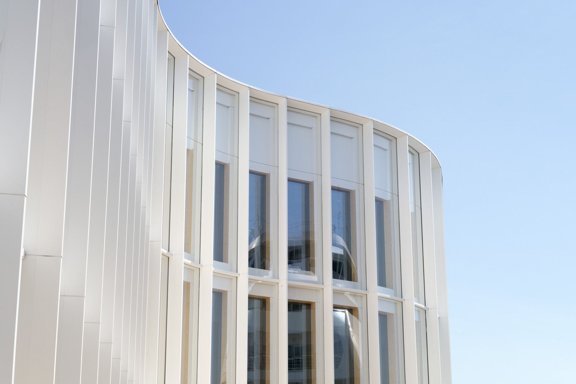 Außenaufnahme einer Gebäudekante mit weißer, geschwungener Pfostenriegelfassade und großflächiger Verglasung.