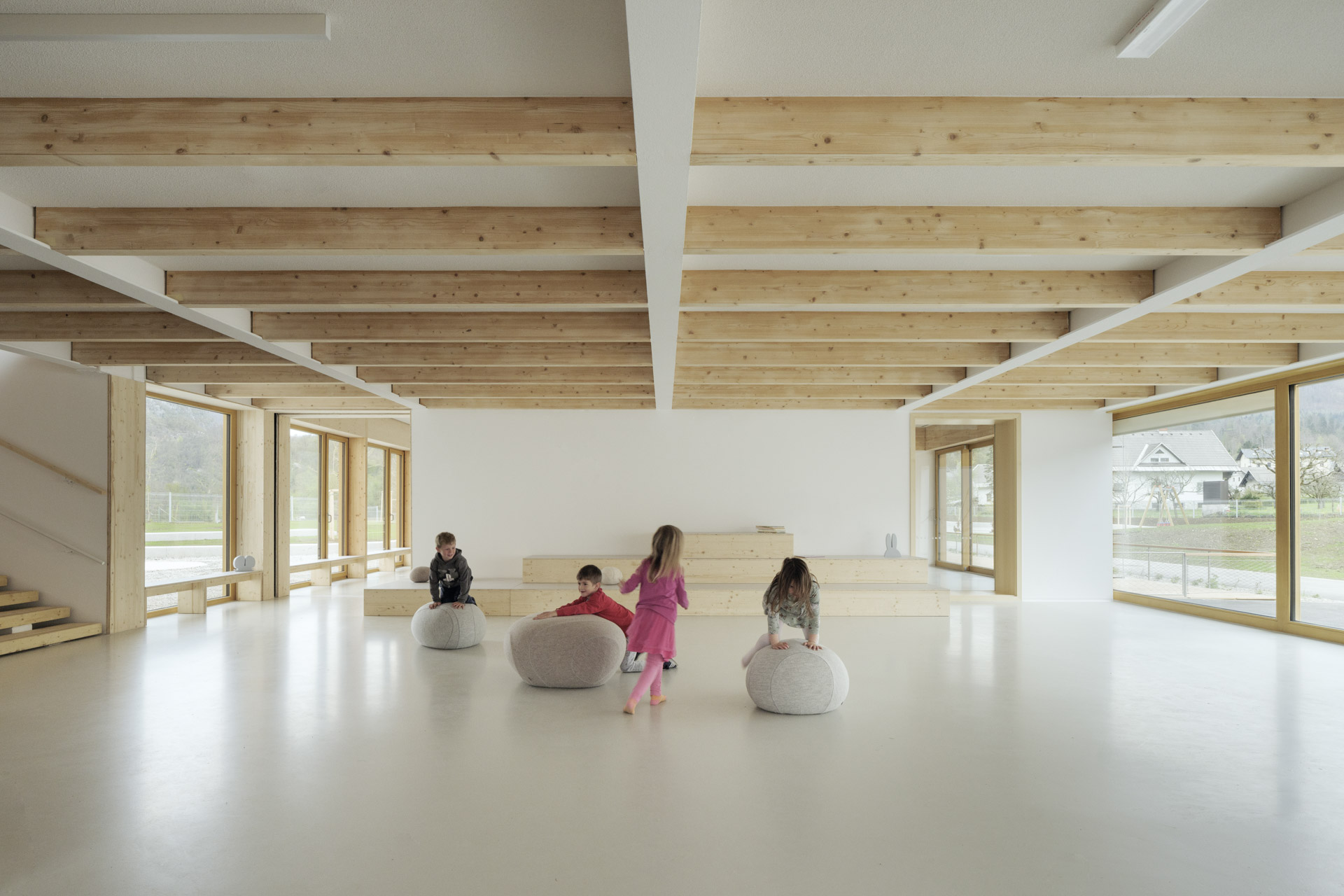 Gebäudeinneres mit offenem Foyer, spielenden Kindern, sichtbarer Holzkonstruktion und hellem Raum.