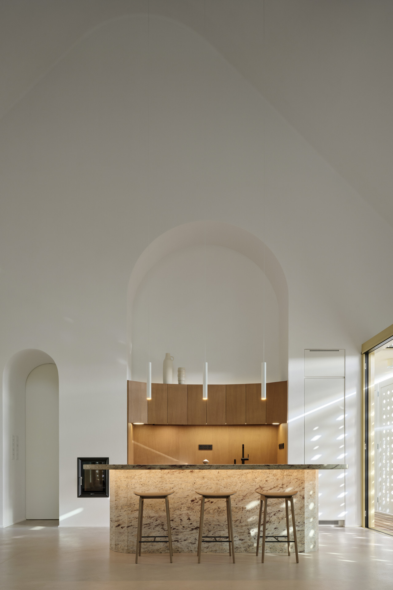Innenraum mit Kücheninsel, abgerundeten Formen und Bögen, durchflutet von Sonnenlicht.