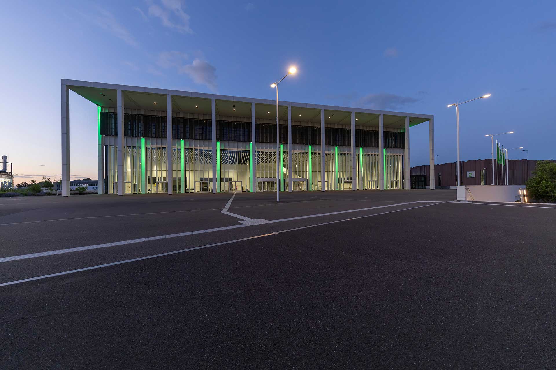 Beleuchtete Messehalle bei Nacht vor einem leeren Platz mit hohen Leuchten.