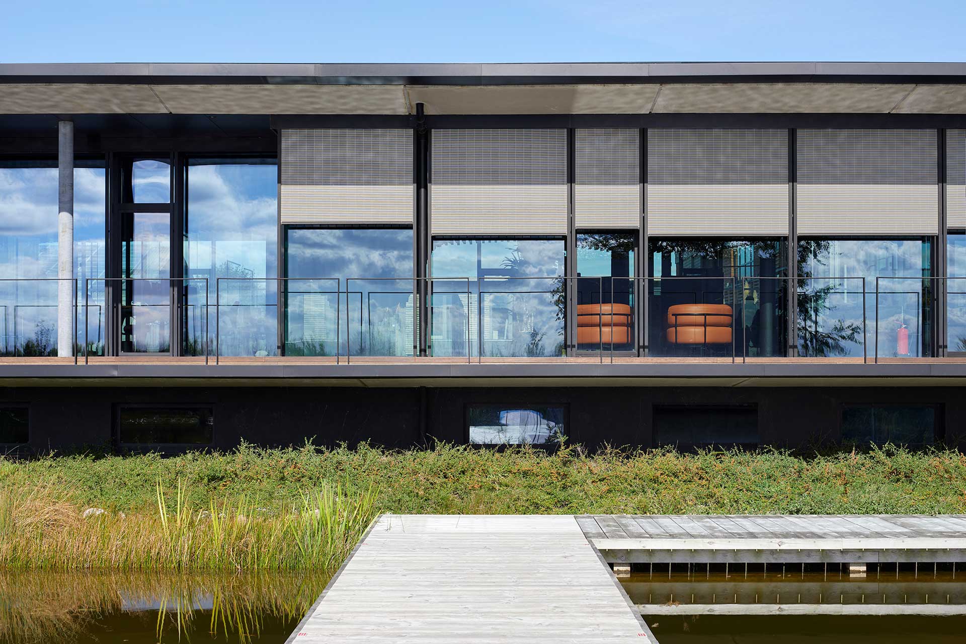 Geb&auml;ude mit Flachdach an einem See. Sonnenjalousien sind halb heruntergelassen.