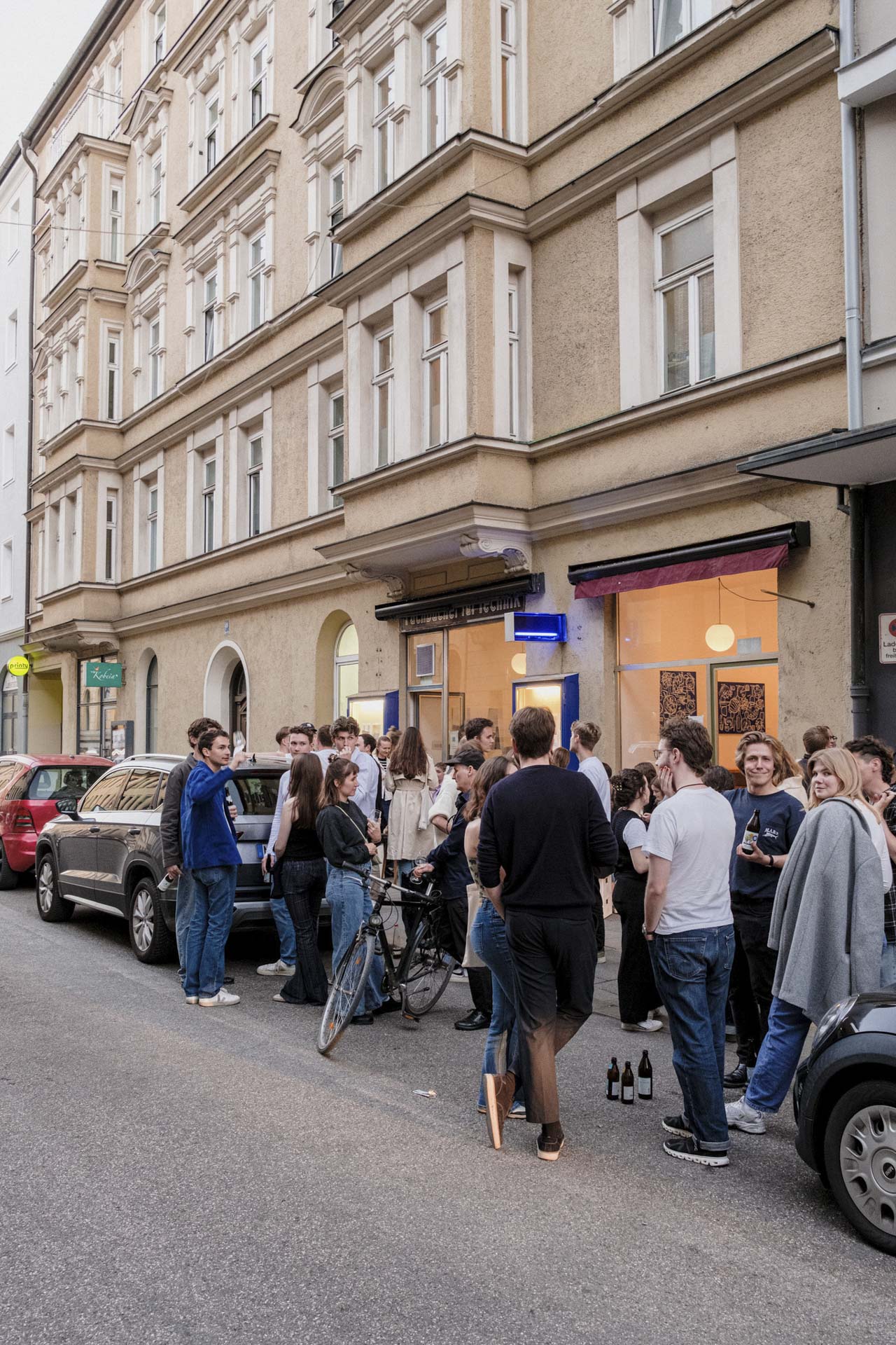 Menschenmenge versammelt sich auf der Straße vor einer Galerie mit großen Fenstern.