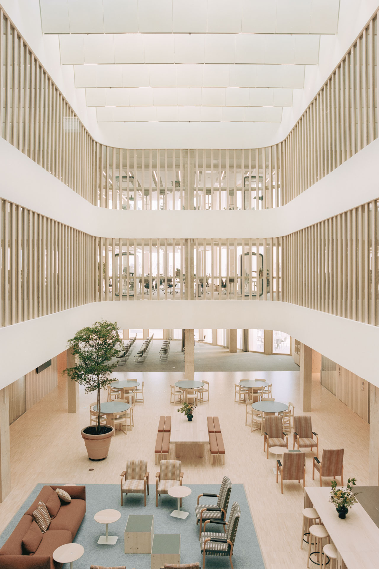 Gebäudeinneres mit mehrgeschossigem Atrium, Lobby mit variabler Bestuhlung, heller Raum mit Holzelementen.