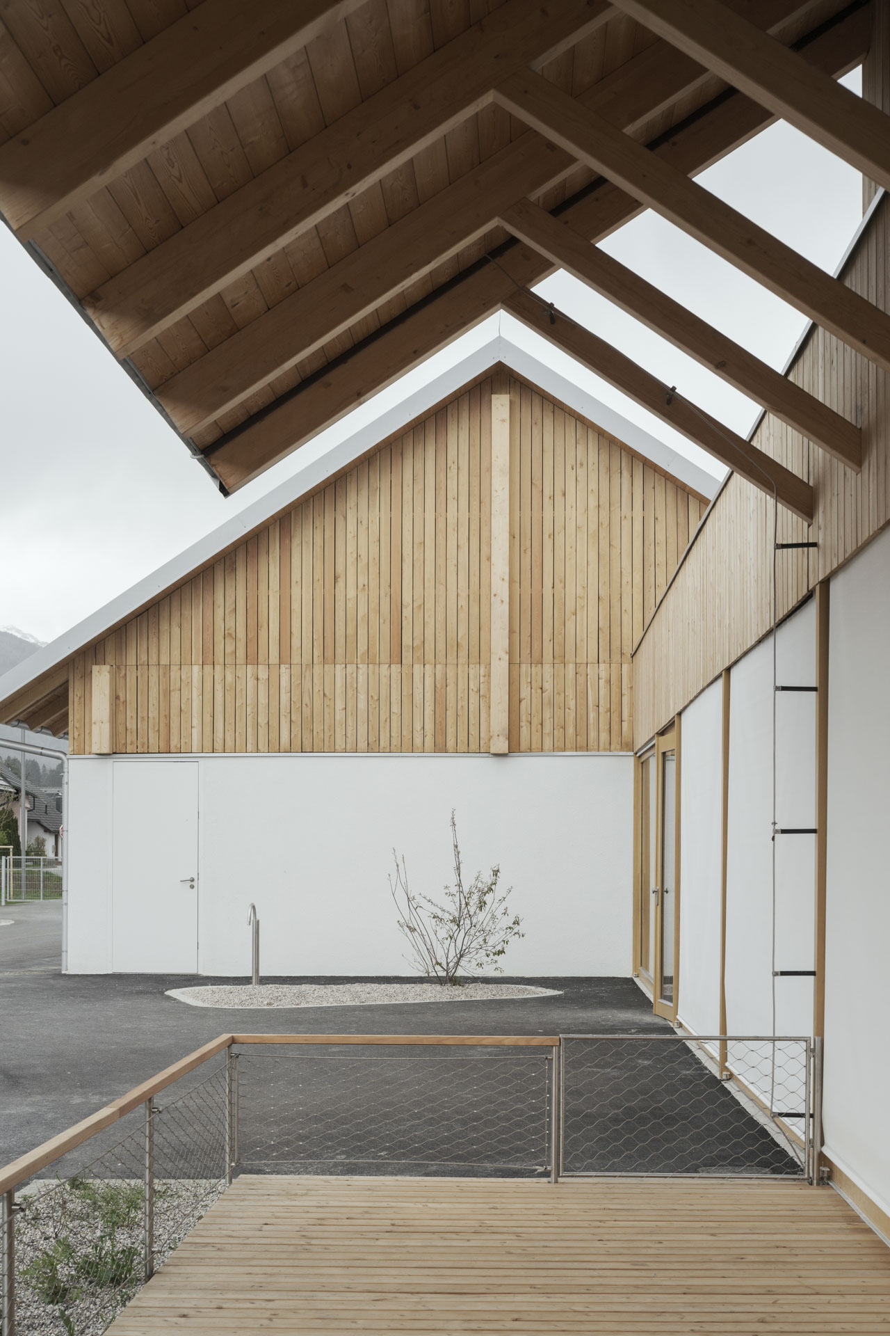 Blick von der Holzterrasse auf das Gebäude mit hellem Erdgeschoss und Holzobergeschoss.