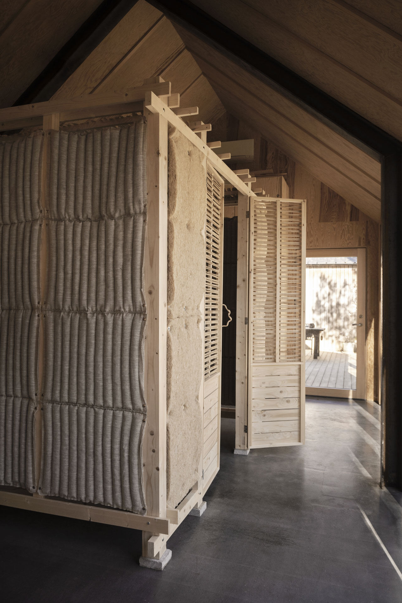 Interior with exposed wood construction, modular wall with textile and pressed insulation, and wooden slatted door.