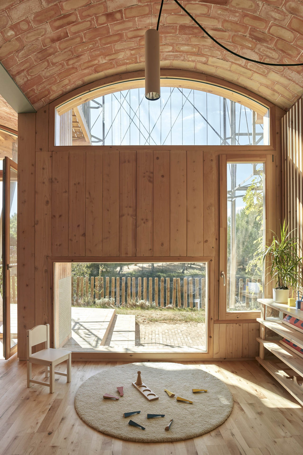 Hoher Innenraum mit Ziegelgewölbe, variierenden Fenstern und rundem Teppich mit verstreuten Buntstiften.