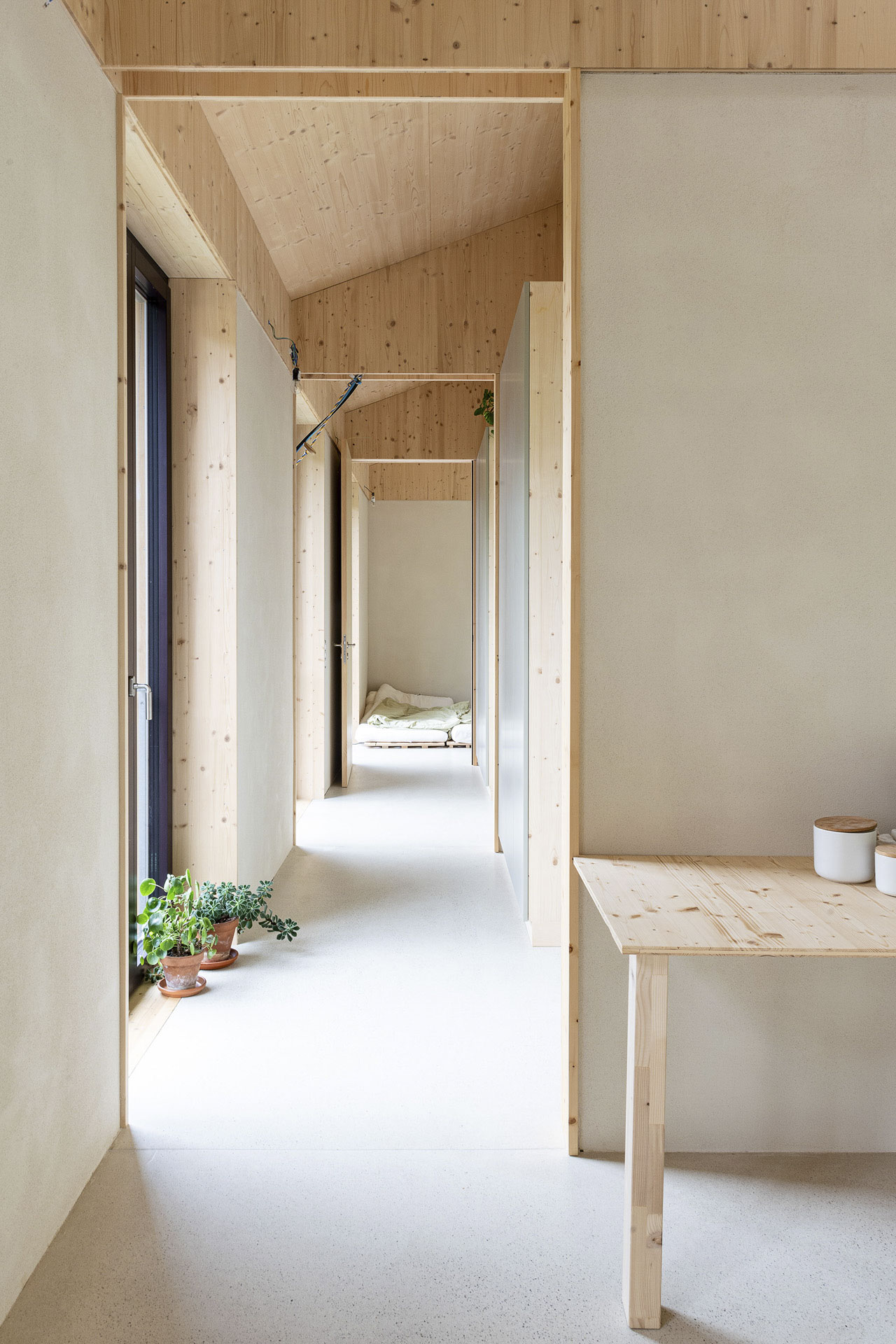 Wohnflur mit Holzoberflächen, seitlicher Verglasung und Ausblick in den anschließenden Schlafraum.