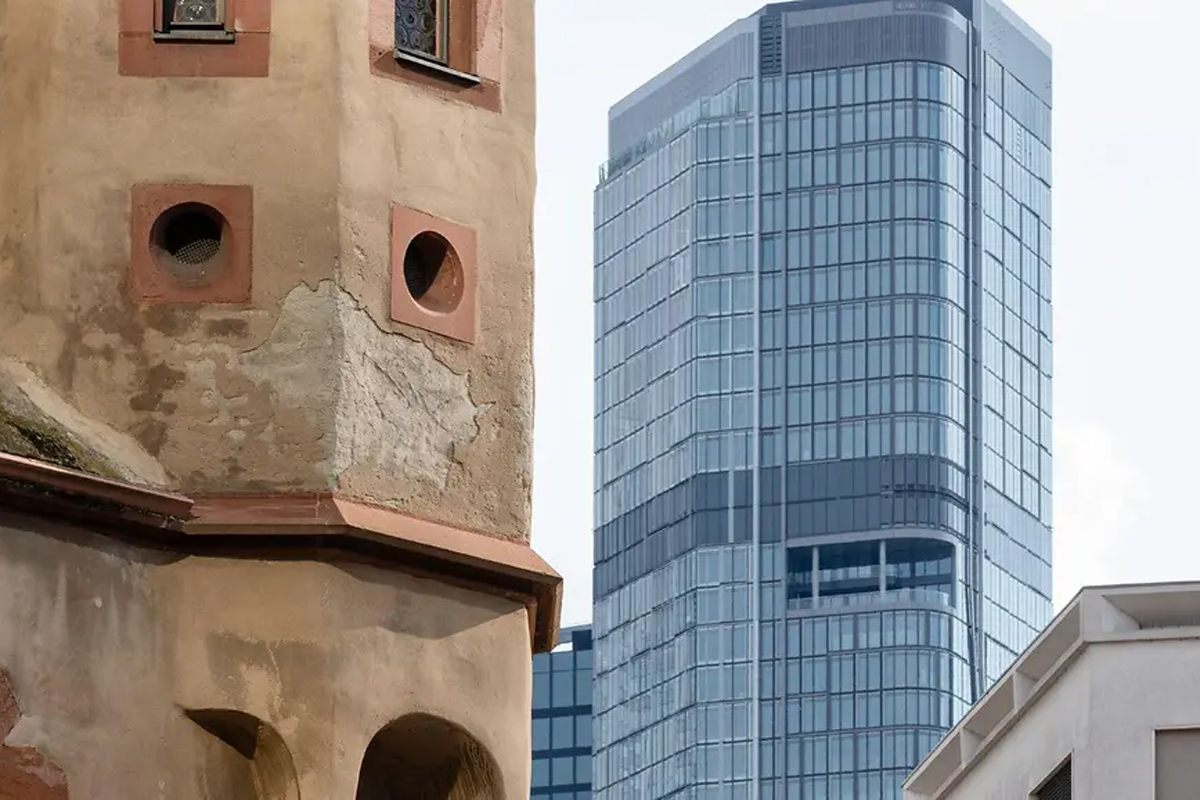 Moderner Glasturm steht neben einem &auml;lteren Turm aus Stein.