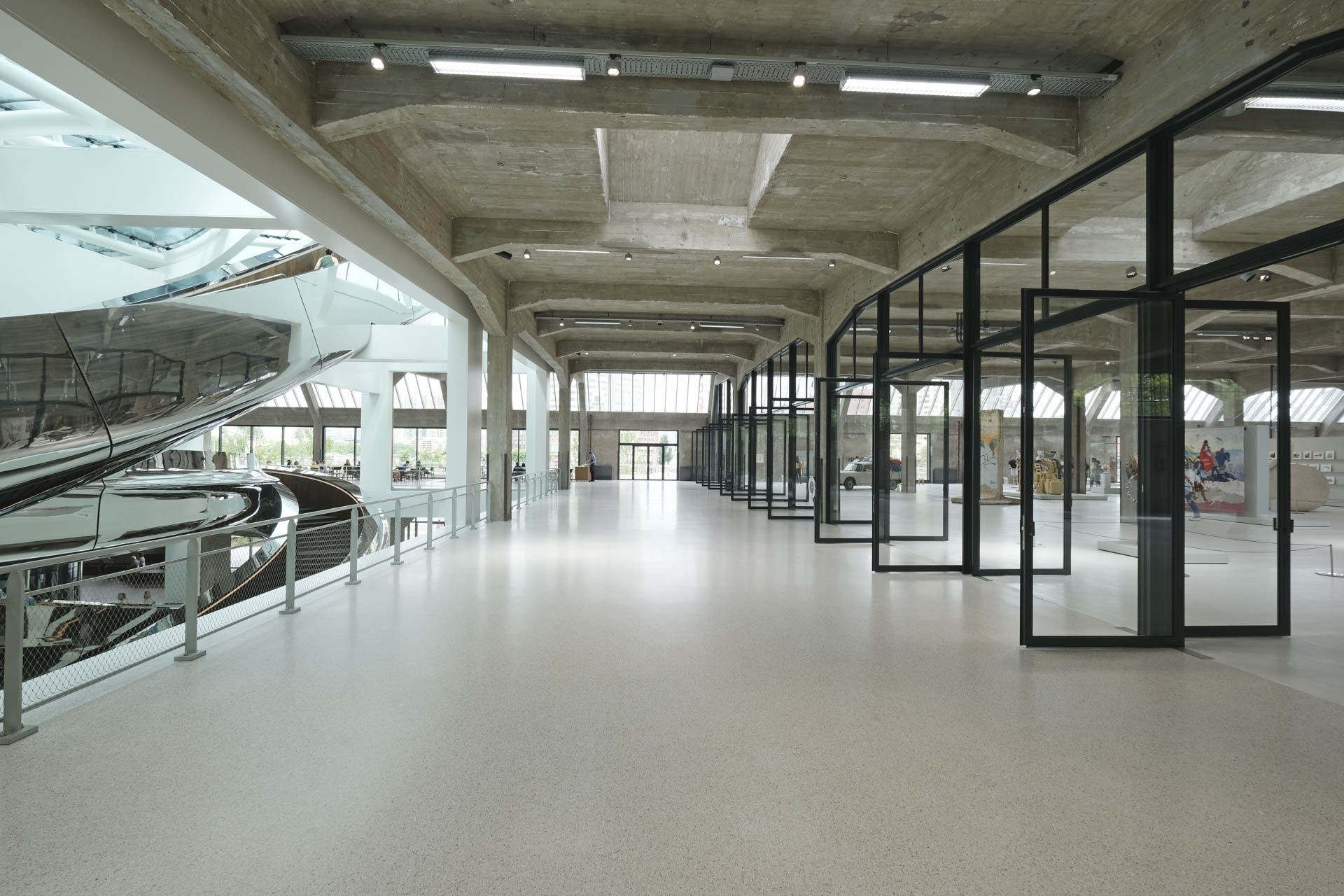 Light-flooded corridor with glass doors on the left, atrium opening on the right, metal ramp visible on the right.