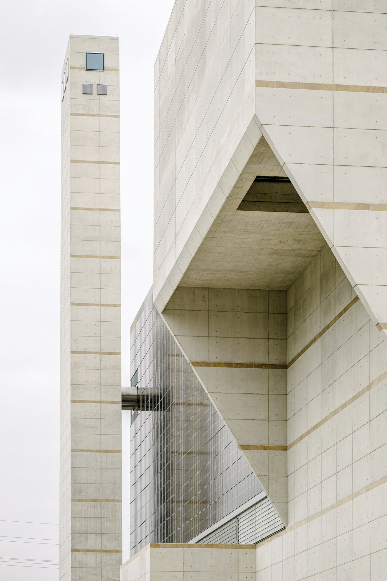 Geometrische Betonstrukturen mit feinen Linien, Einschnitten und vertikaler Betonung; horizontale Schichtungen verstärken die Massivität des Baukörpers.