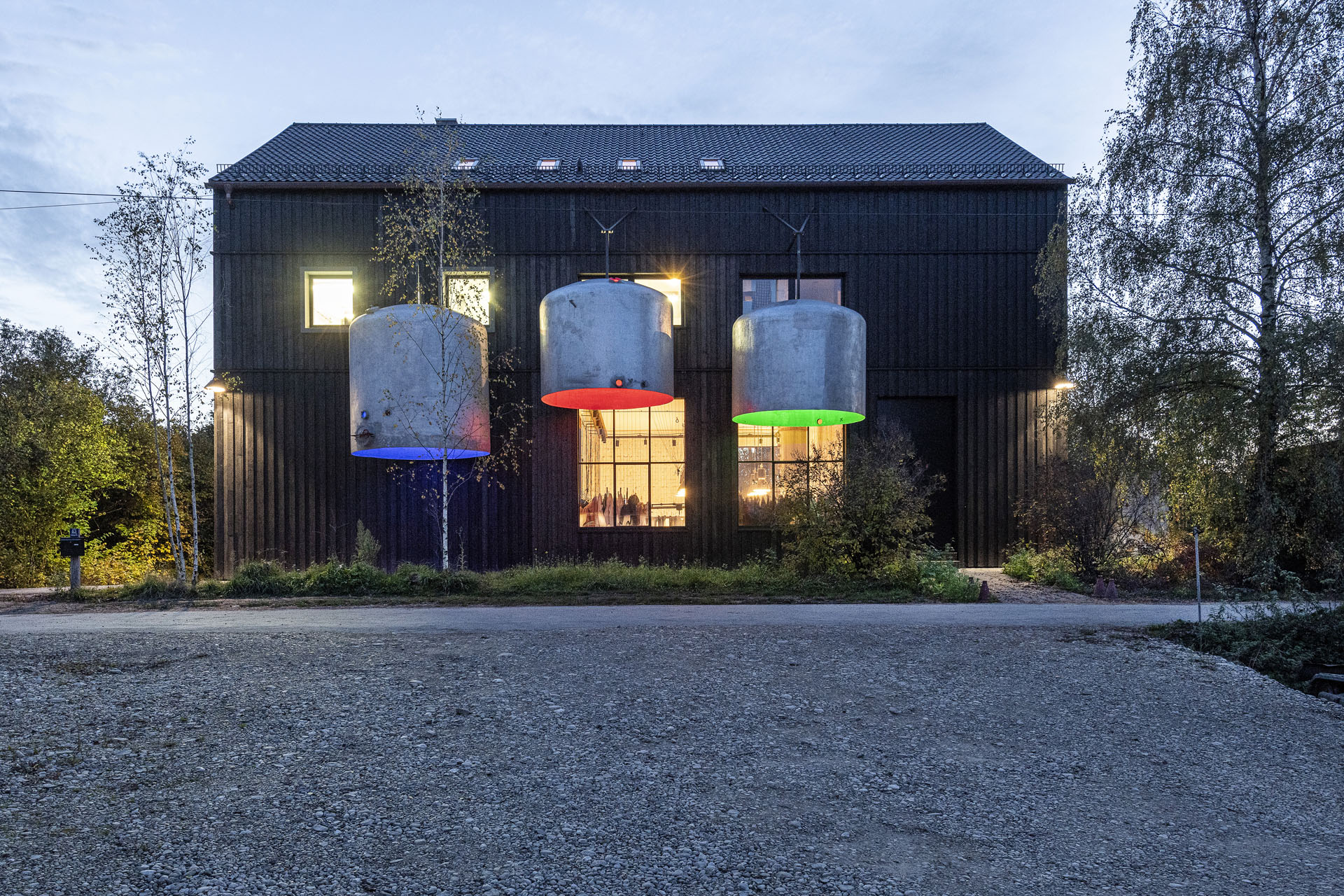 Holzvertäfelte Eingangsfassade eines Hauses. Davor hängen drei riesige Lampenschirme.