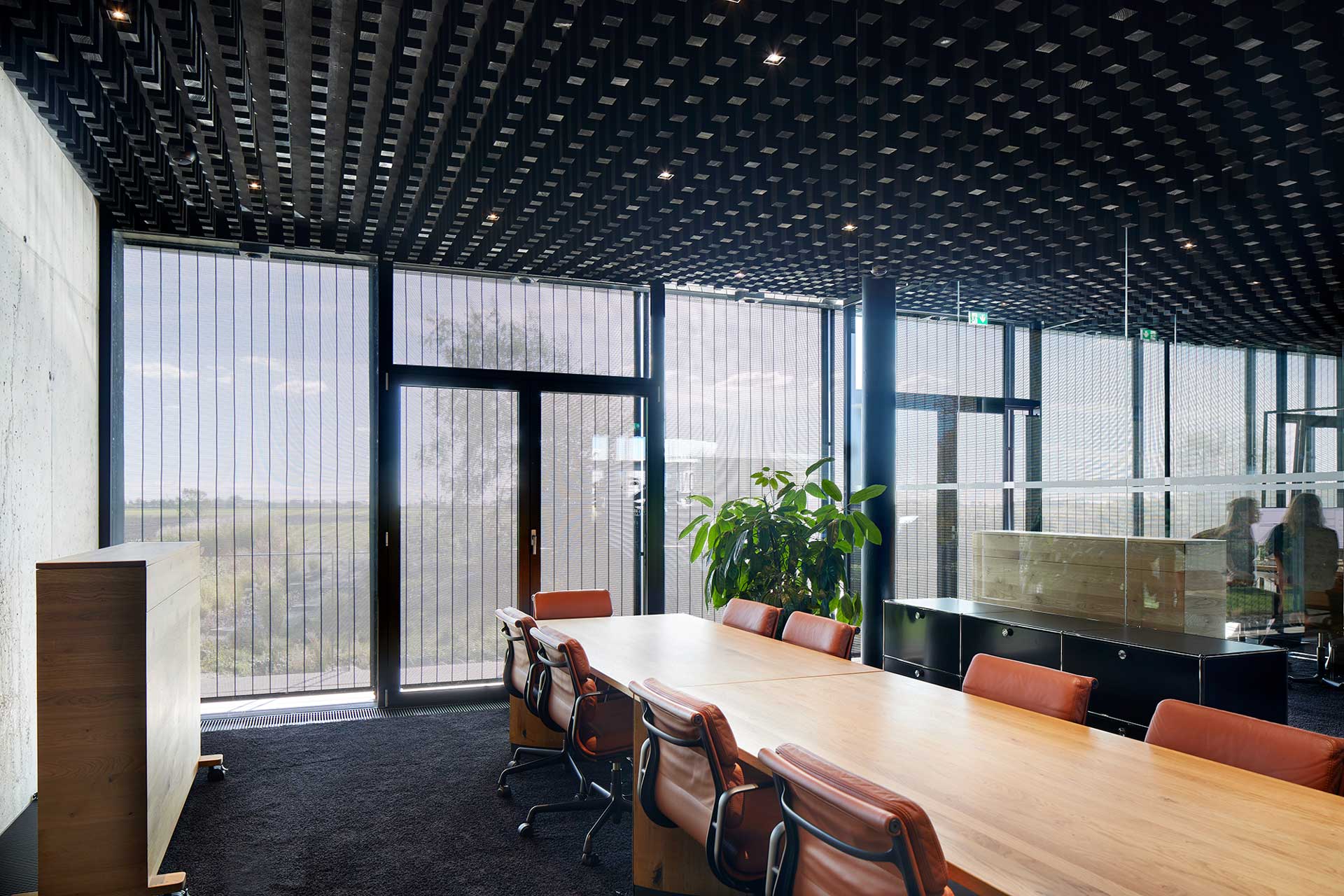 Meetingraum mit langem Tisch und Lederst&uuml;hlen. Die bodentiefen Fenster sind mit Jalousien verdunkelt.