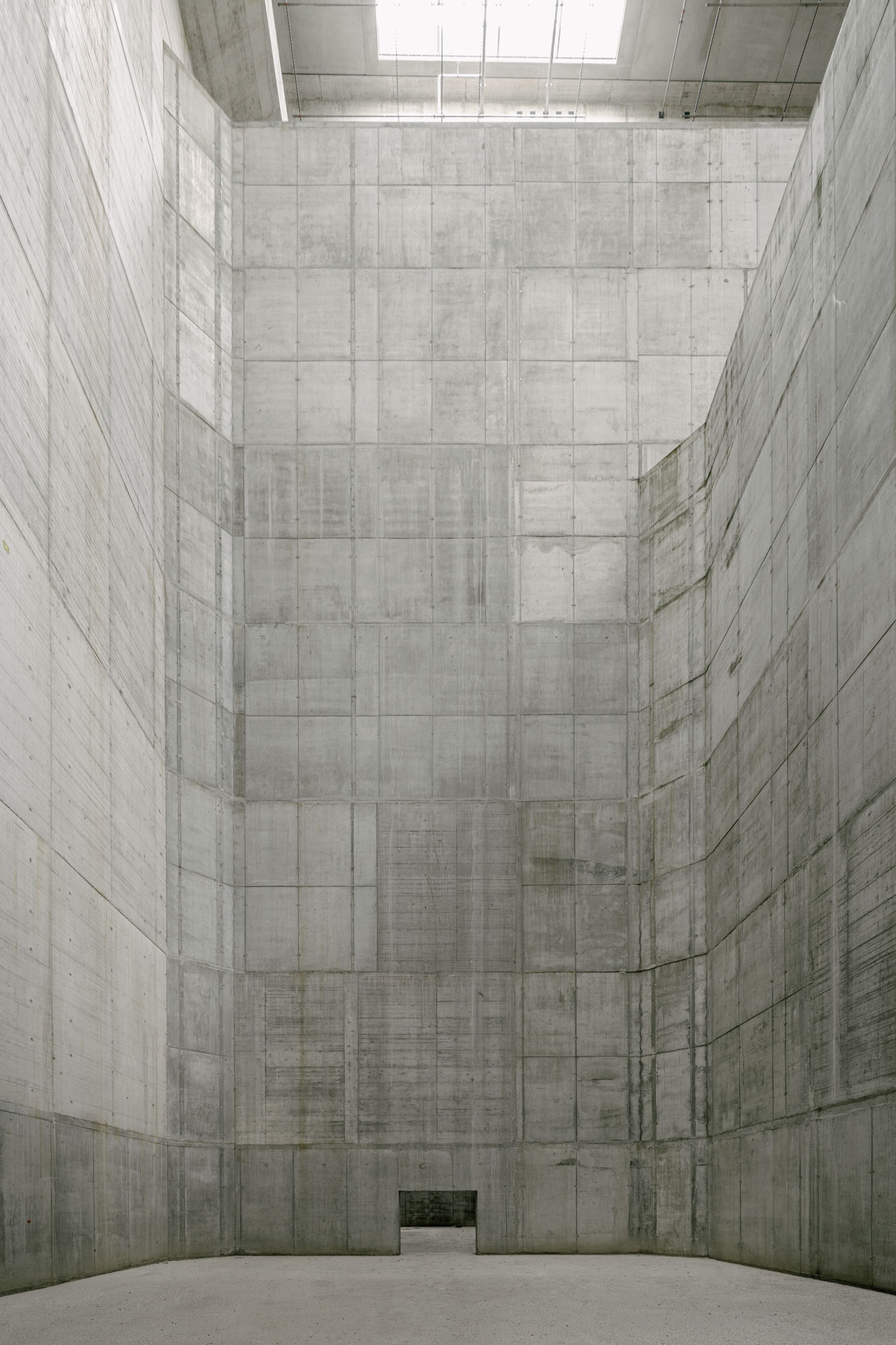 Extrem hoher Raum mit Stahlbetonwänden, Schalungsspuren und Tageslichtöffnung im Dach.