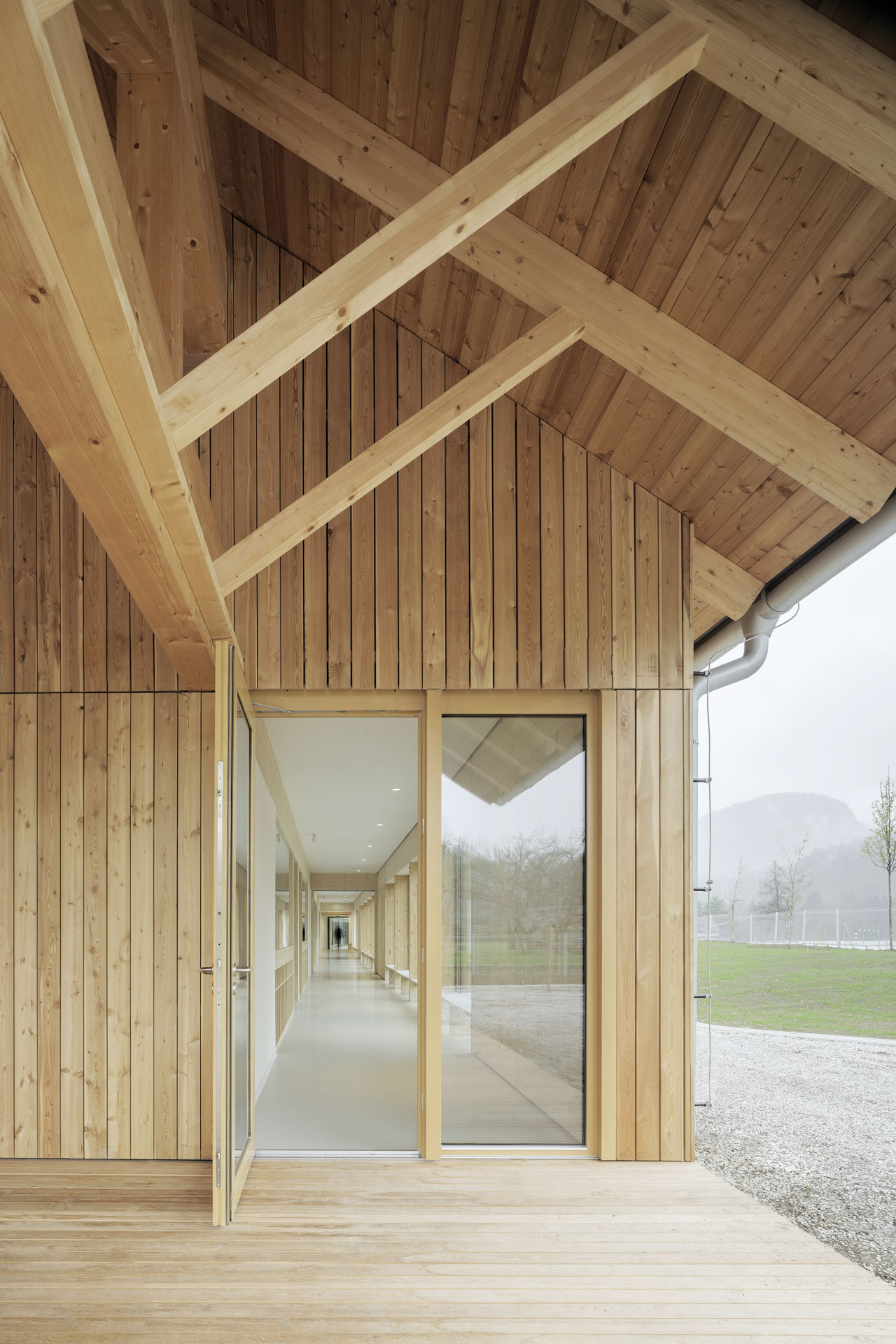 Eingangssituation mit verglaster Tür, überdachter Holzterrasse und Holzfassade an der Giebelseite des Hauses.