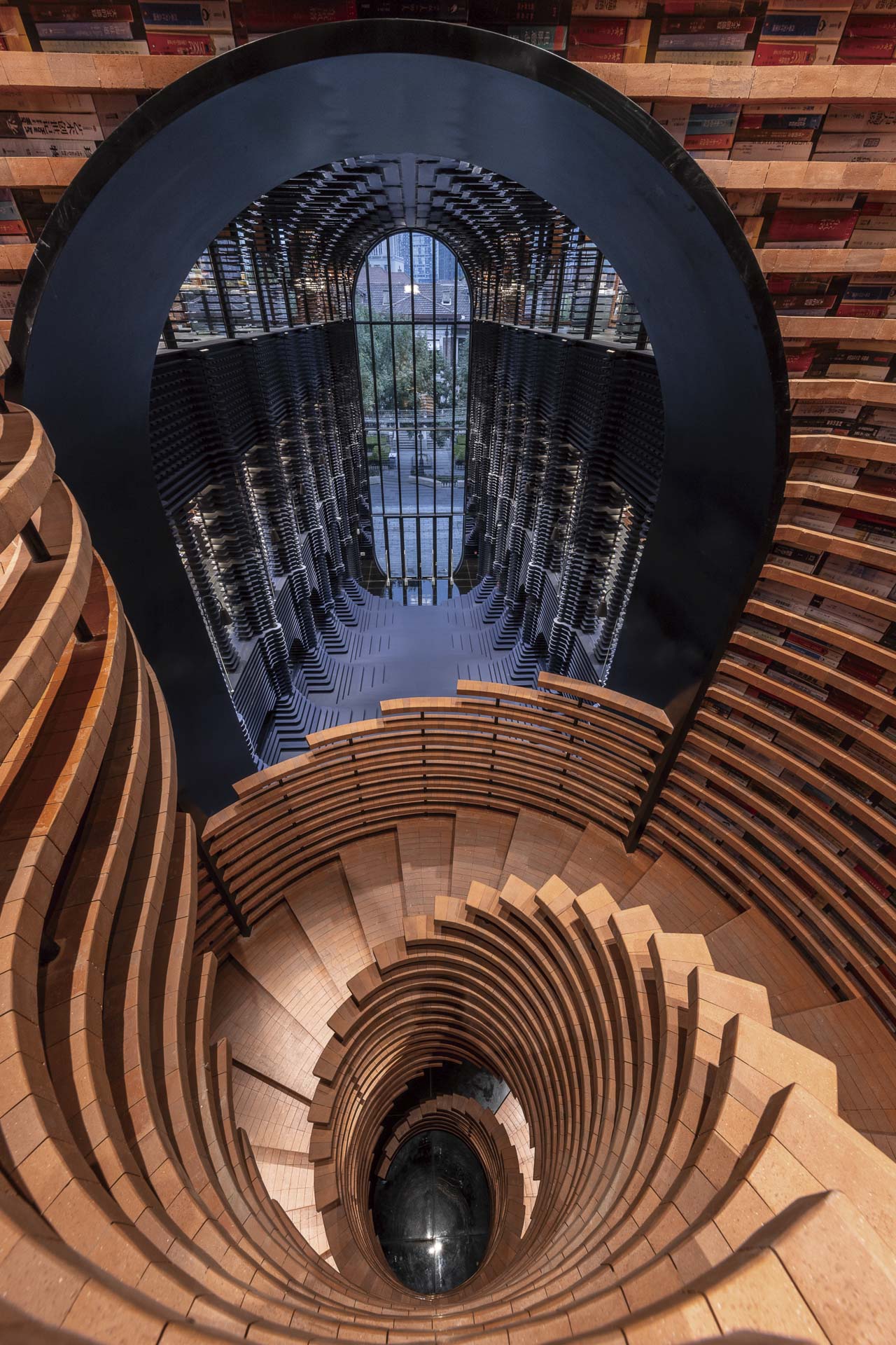 Ovale Ziegeltreppe über mehrere Geschosse, Wände als Bücherregale, große Öffnung mit Blick auf mehrgeschossiges Fenster.