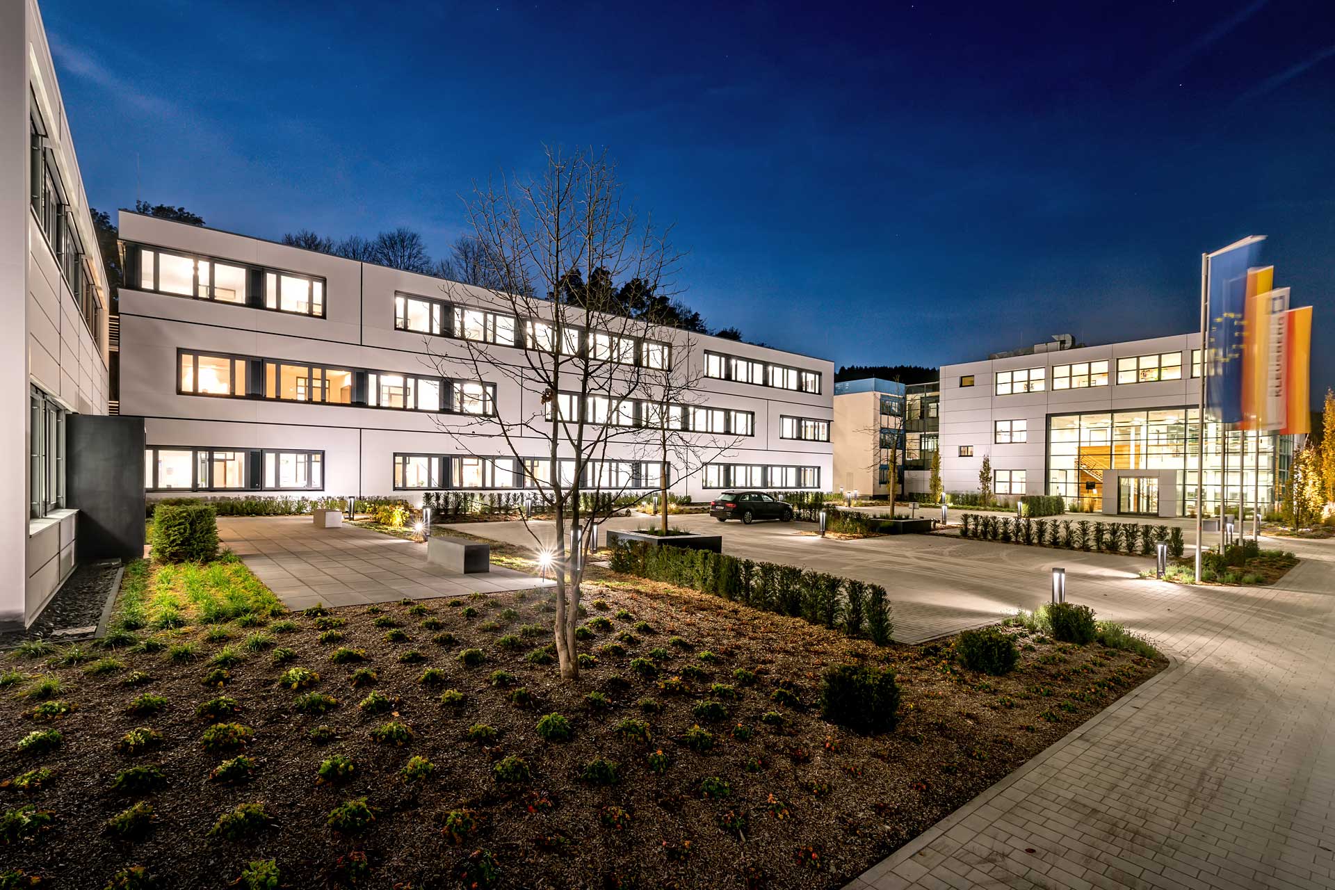 Beleuchtetes B&uuml;rogeb&auml;ude in der Abentstimmung mit einem geplegten Innenhof mit Sitzm&ouml;glichkeiten.