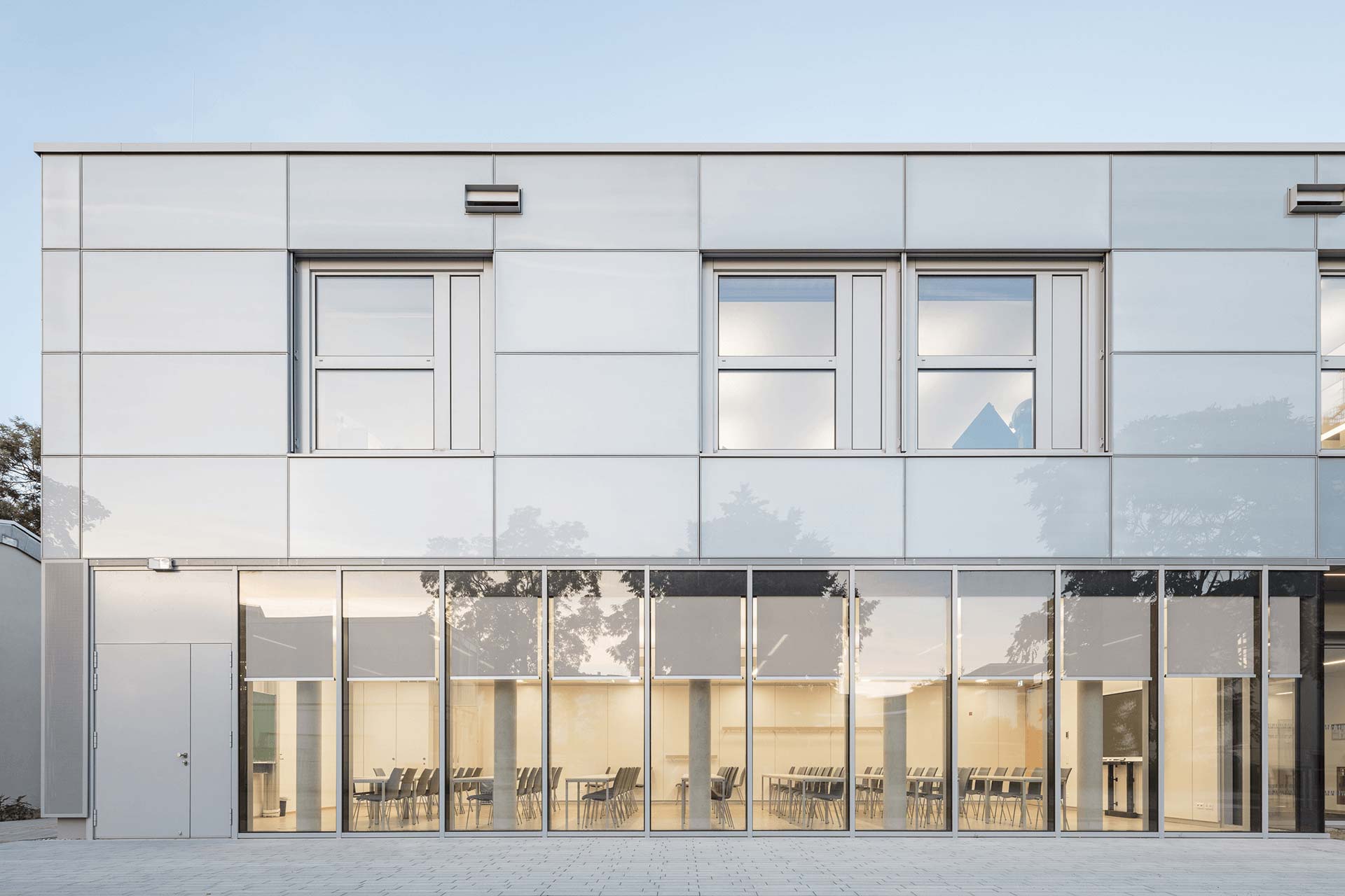 Fassade eines Bürogebäudes mit viel Glas. Davor ist ein Platz mit Sitzflächen und Pflanzen.