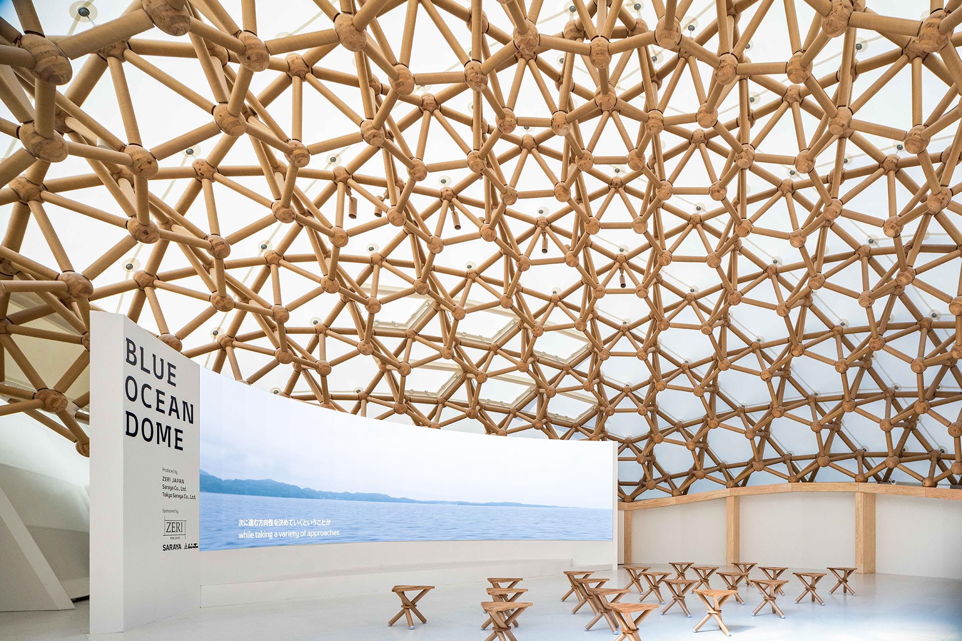 Panels arranged in a mosaic pattern in warm orange tones, in a busy exhibition space with high ceilings.