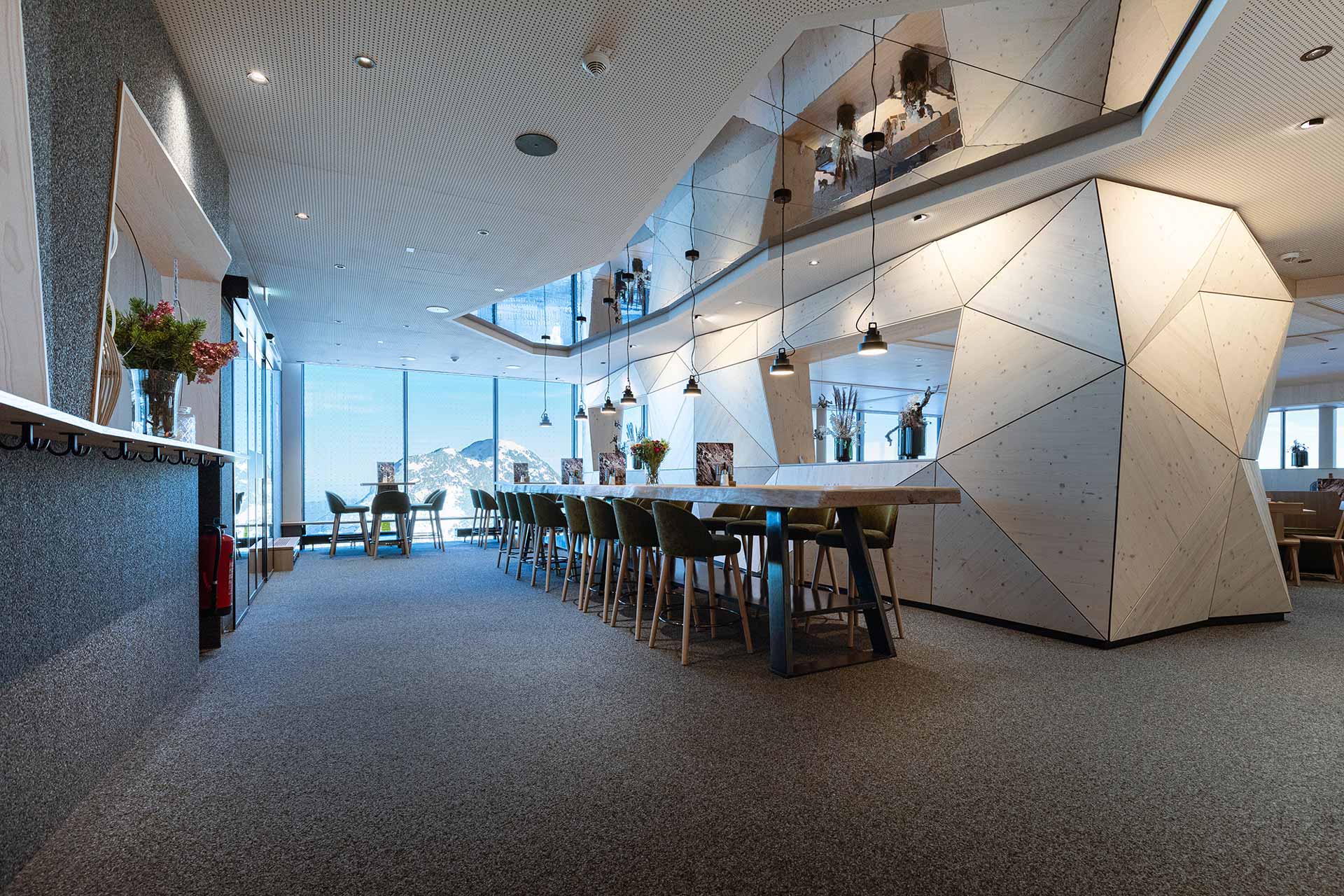 Bergrestaurant mit moderner Einrichtung und einem langen Tisch vor einem Tresen.