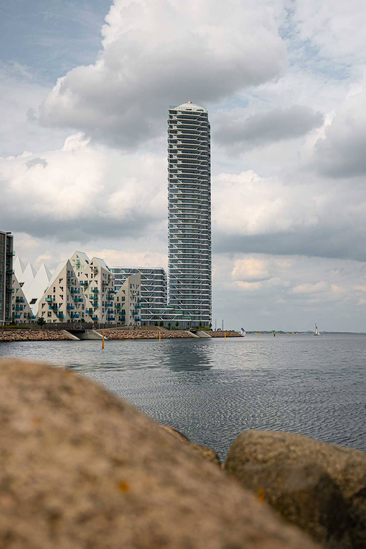 Schlankes Hochhaus am Ufer neben anderen Mehrfamilienhäusern. 