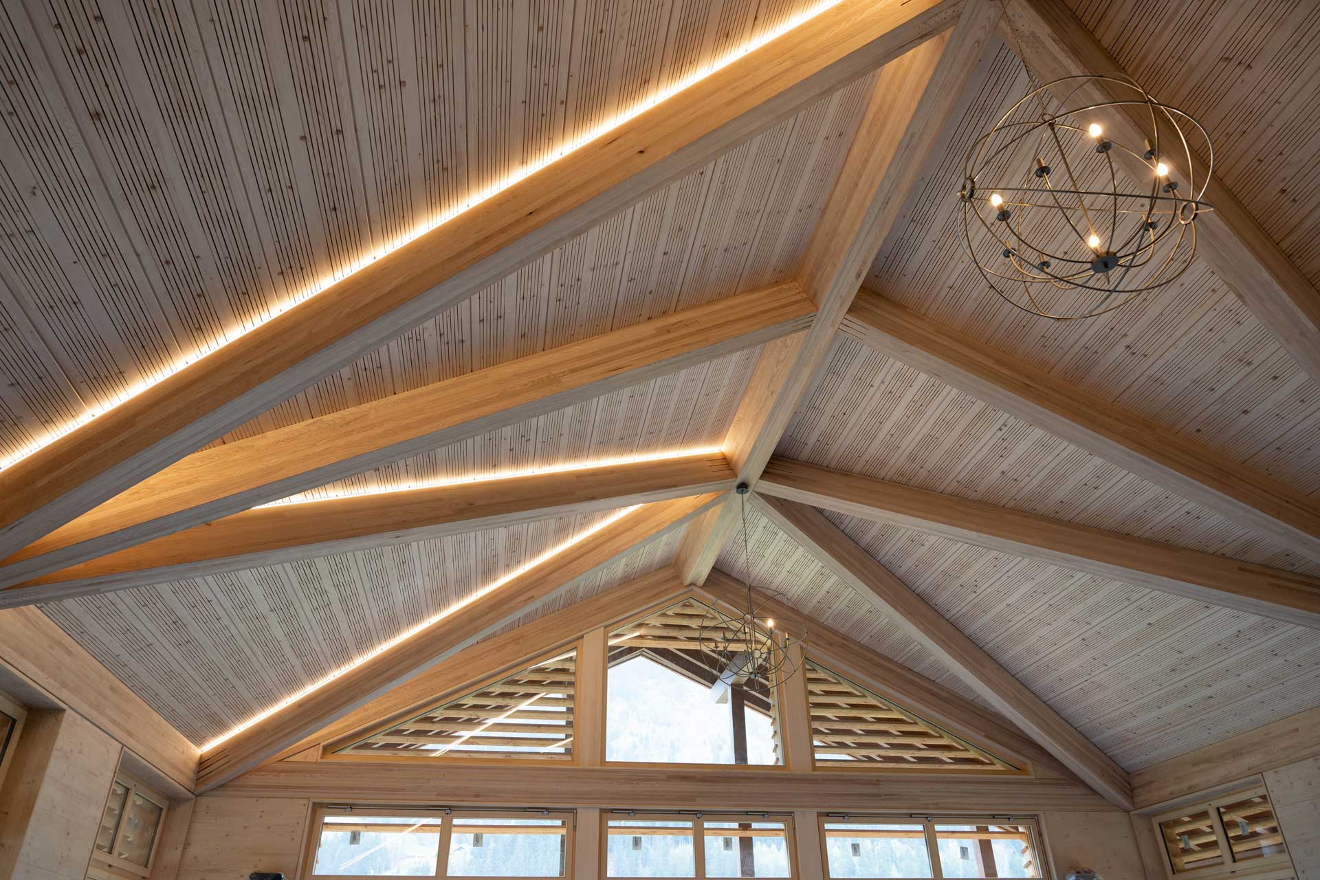 V-förmig zulaufende Holzdecke mit breiten Holzbalken und einer Leuchte.