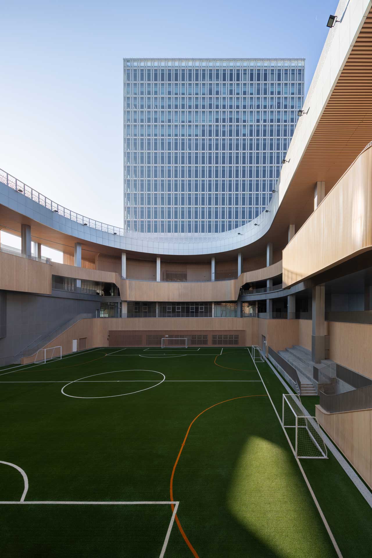 Football pitch surrounded by wooden spectator stands. A high-rise building can be seen in the background.