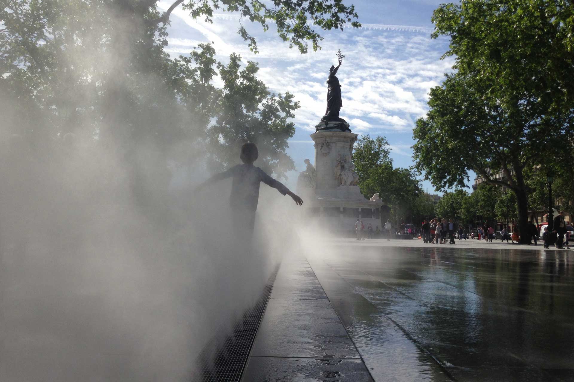 Ein Kind spielt in einem Brunnen an einem Platz in der Stadt.