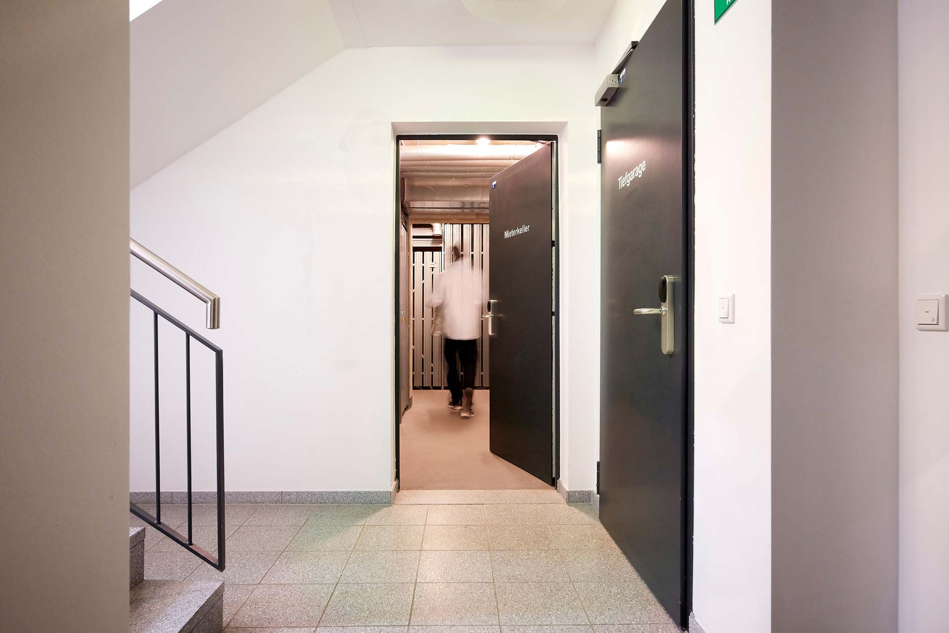 Keller eines Mehrfamilienhauses mit offener Tür zur Garage, durch die ein Mann geht.