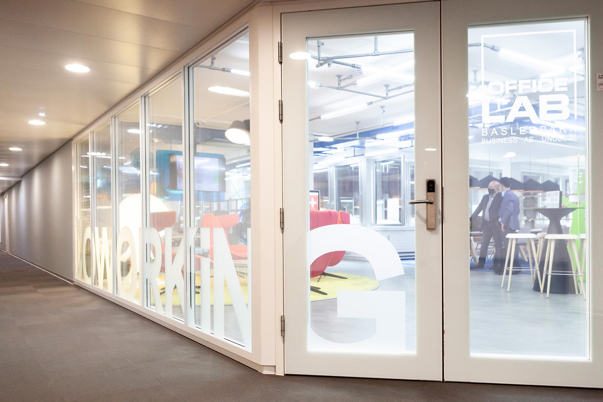 B&uuml;rogang mit grauem Fu&szlig;boden. Das Eckb&uuml;ro wird durch eine Glaswand abgegrenzt.